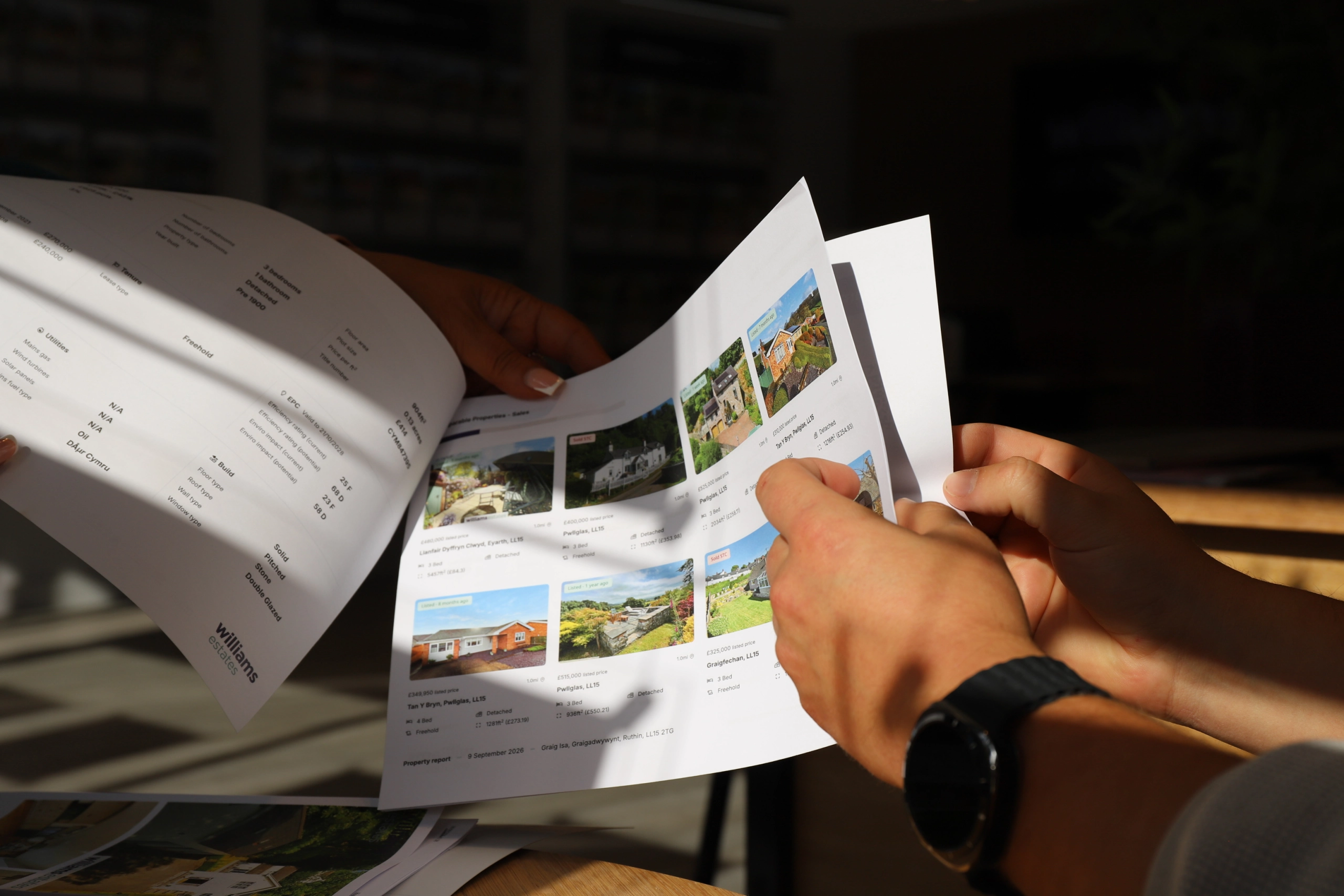 Hands holding open a property brochure showing multiple photographs of houses and gardens