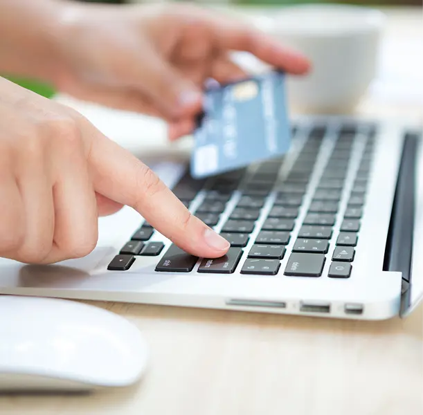 Hand typing on laptop keyboard while another hand holds a blue credit card
