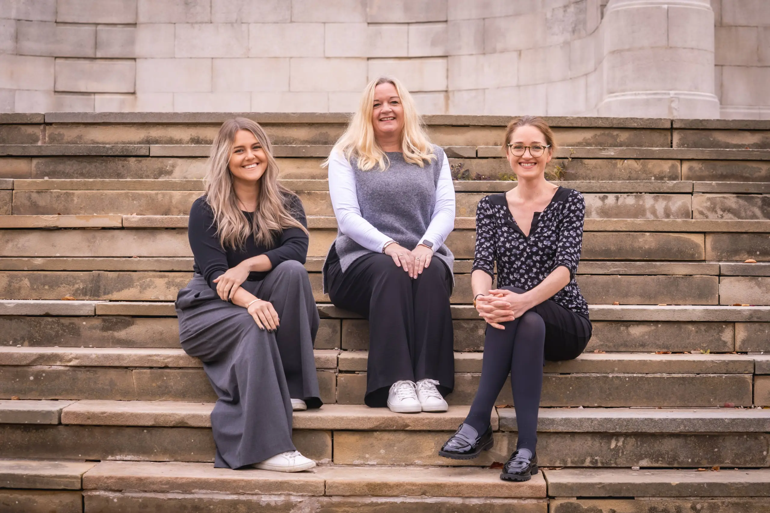 Three female Redbrik Property Consultants sitting on stone steps in front of Chesterfield Town Hall