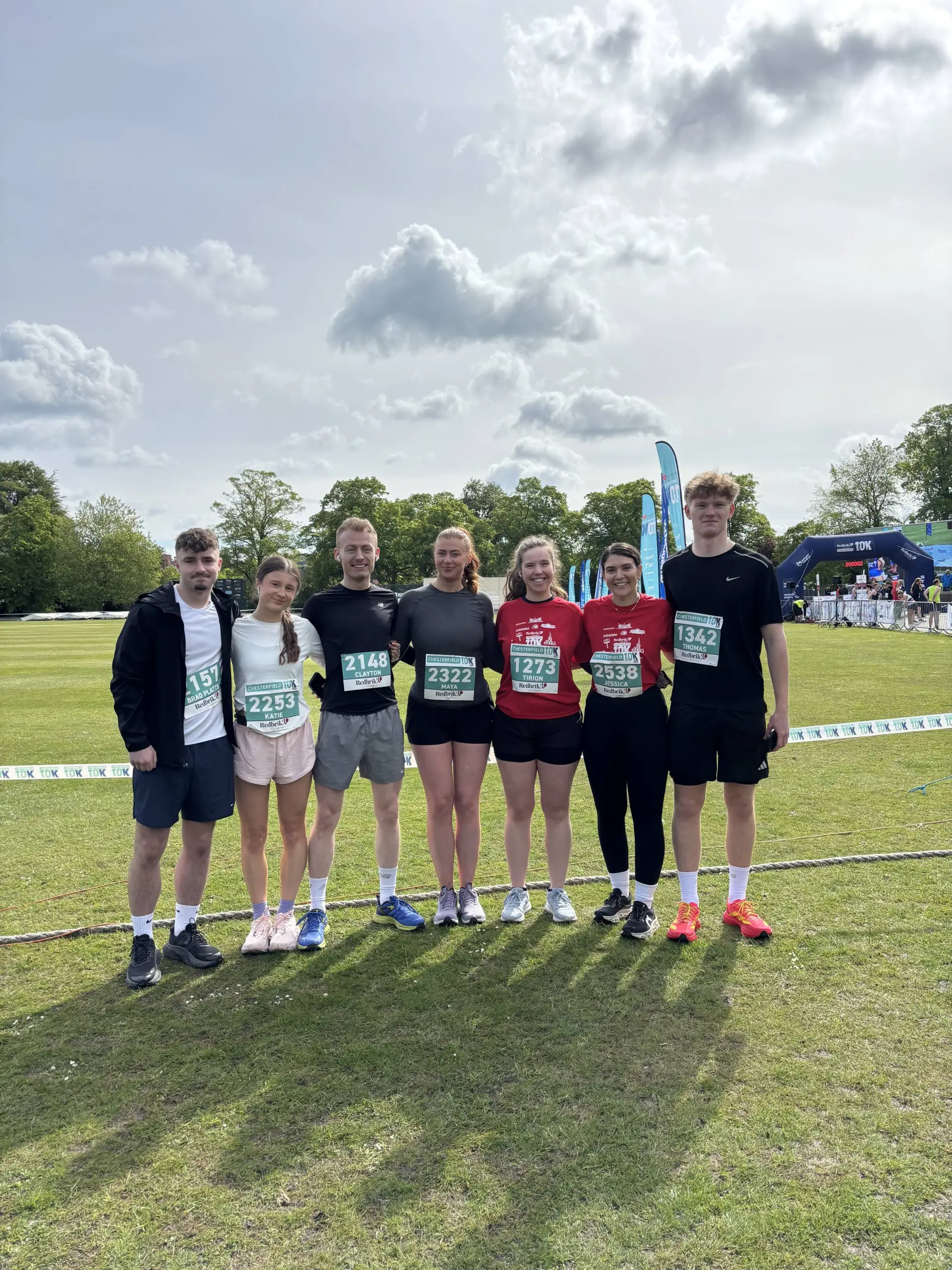 Seven people wearing race bibs standing on a grass field at a 10K event