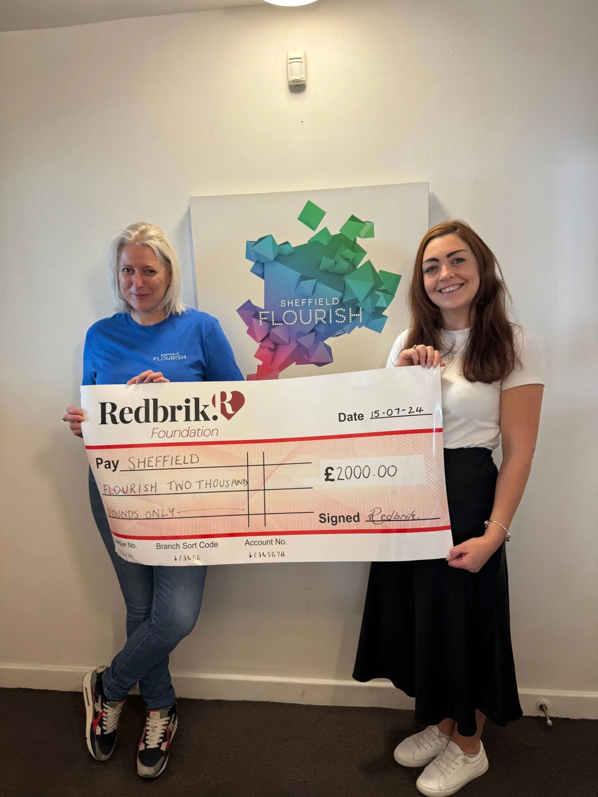 Two women holding a large Redbrick Foundation cheque for £2000.00 payable to Sheffield Flourish, dated 15-07-24