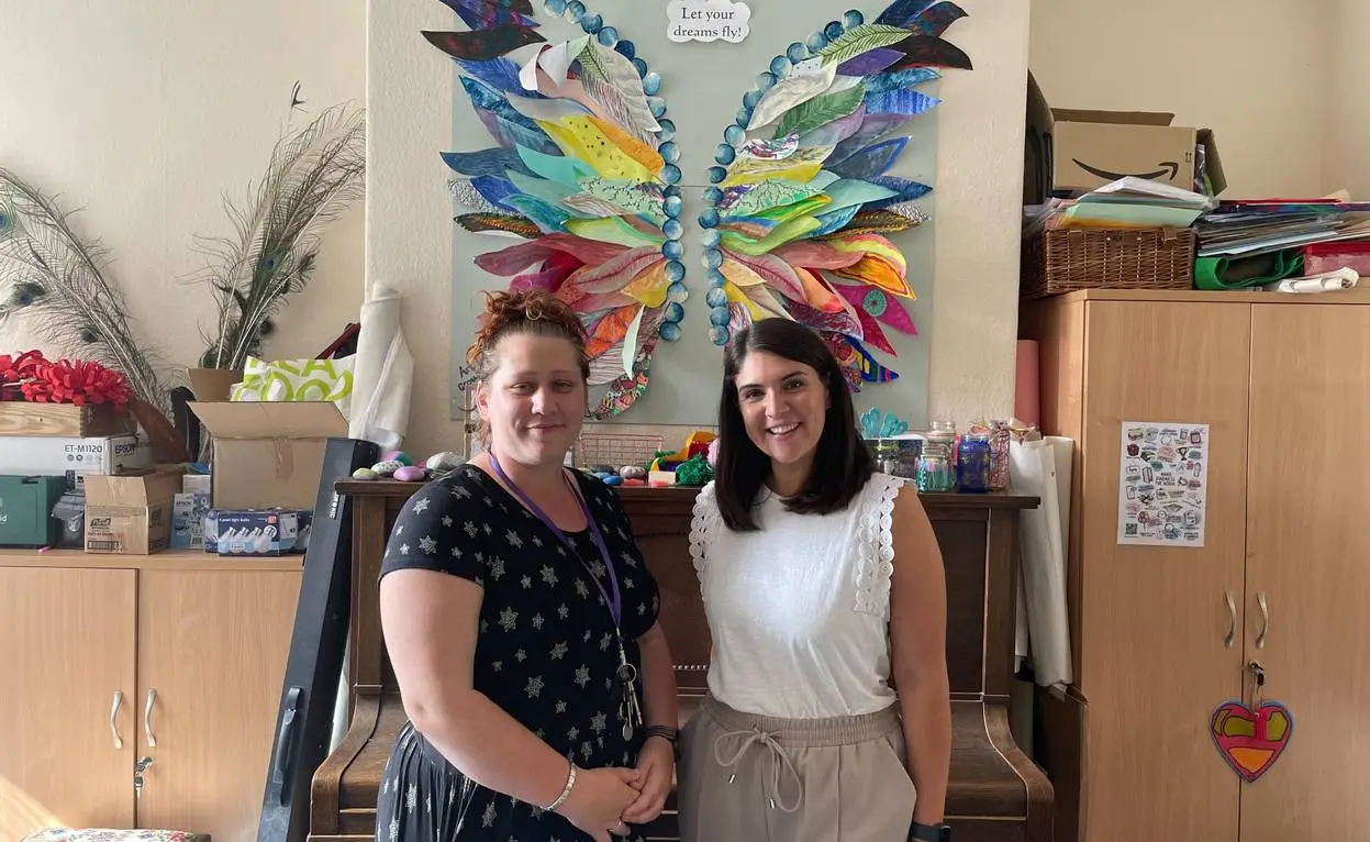 Two women standing in an office with colourful butterfly wall art and "Let your dreams fly" text above