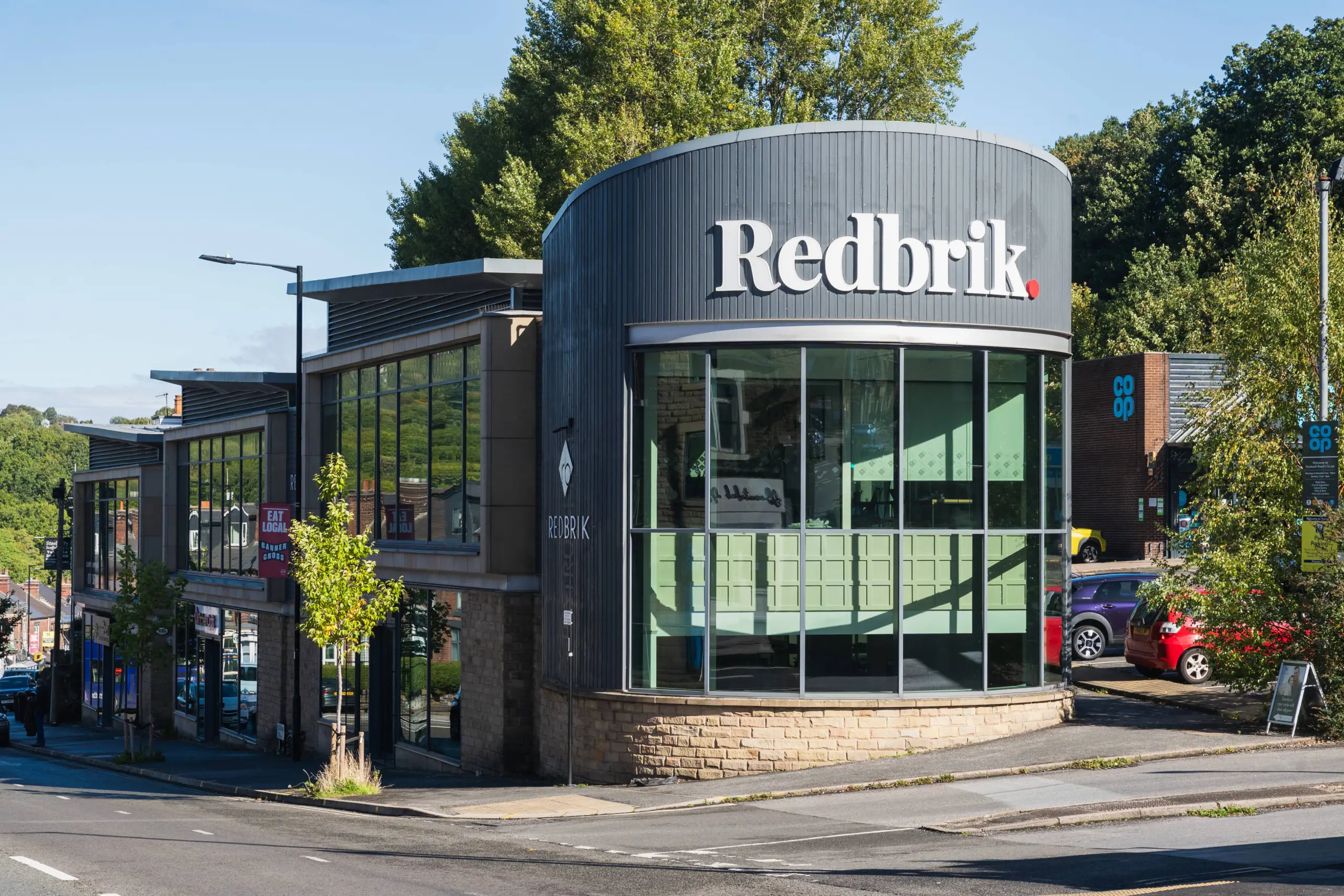 Modern commercial building with "Redbrik" signage, dark corrugated metal cladding, large windows, and brick base