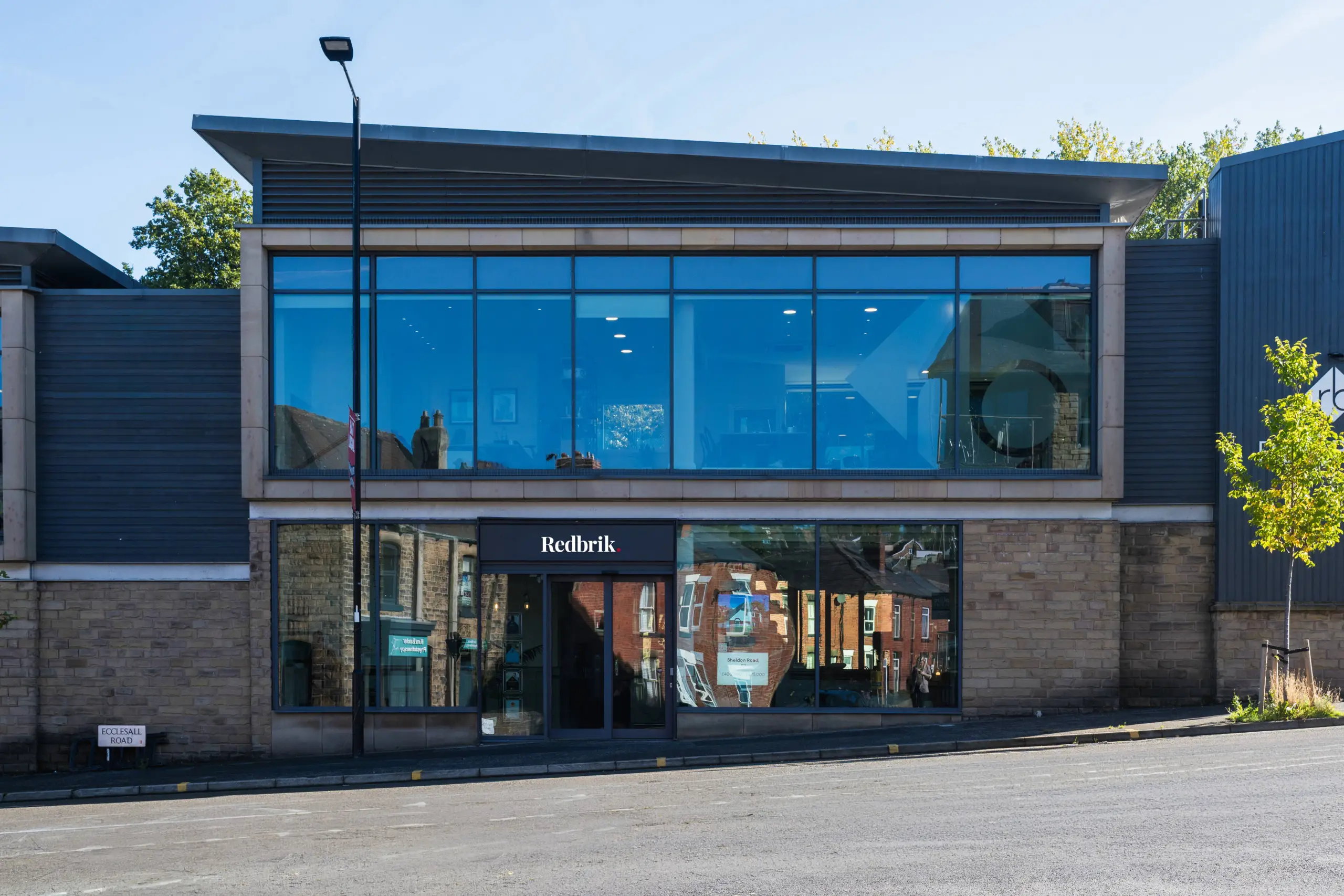Modern two-storey building with blue-tinted glass upper floor and brick lower floor. Ground floor storefront reads "Redbrik" with display windows. Street sign reads "Ecclesale Road".