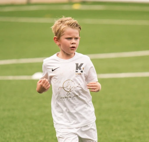 Child in white sports kit running on grass field