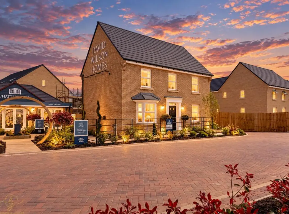 Brick house with "David Wilson Homes" text on gable, illuminated at dusk with sunset sky, show home and landscaping visible