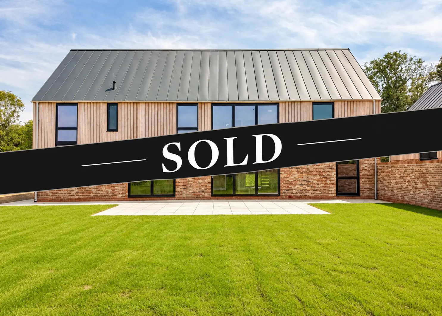 Modern house with metal roof and brick base, "SOLD" banner across the front