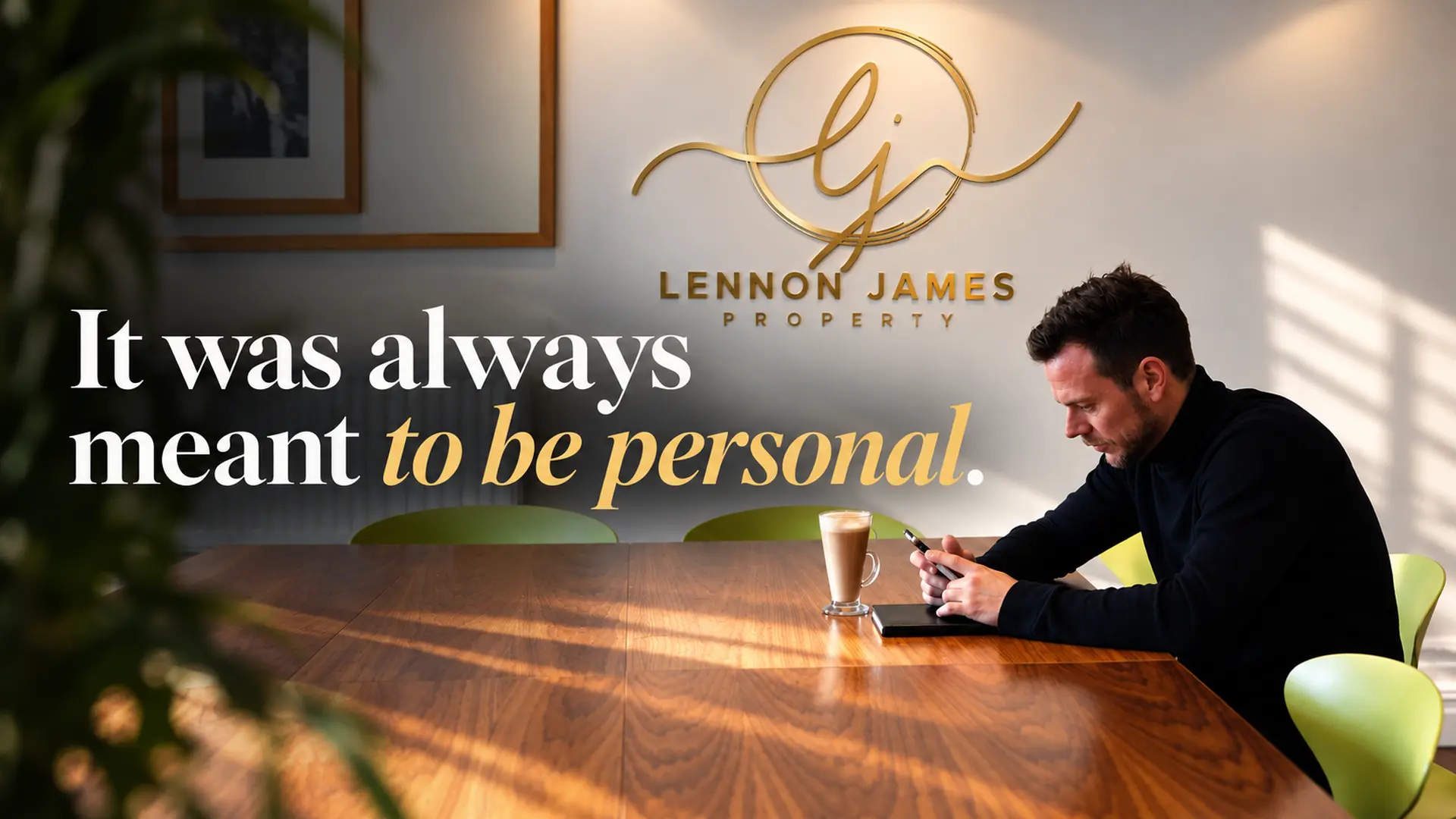 Man sitting at wooden table with coffee, Lennon James Property logo and tagline "It was always meant to be personal" on wall behind