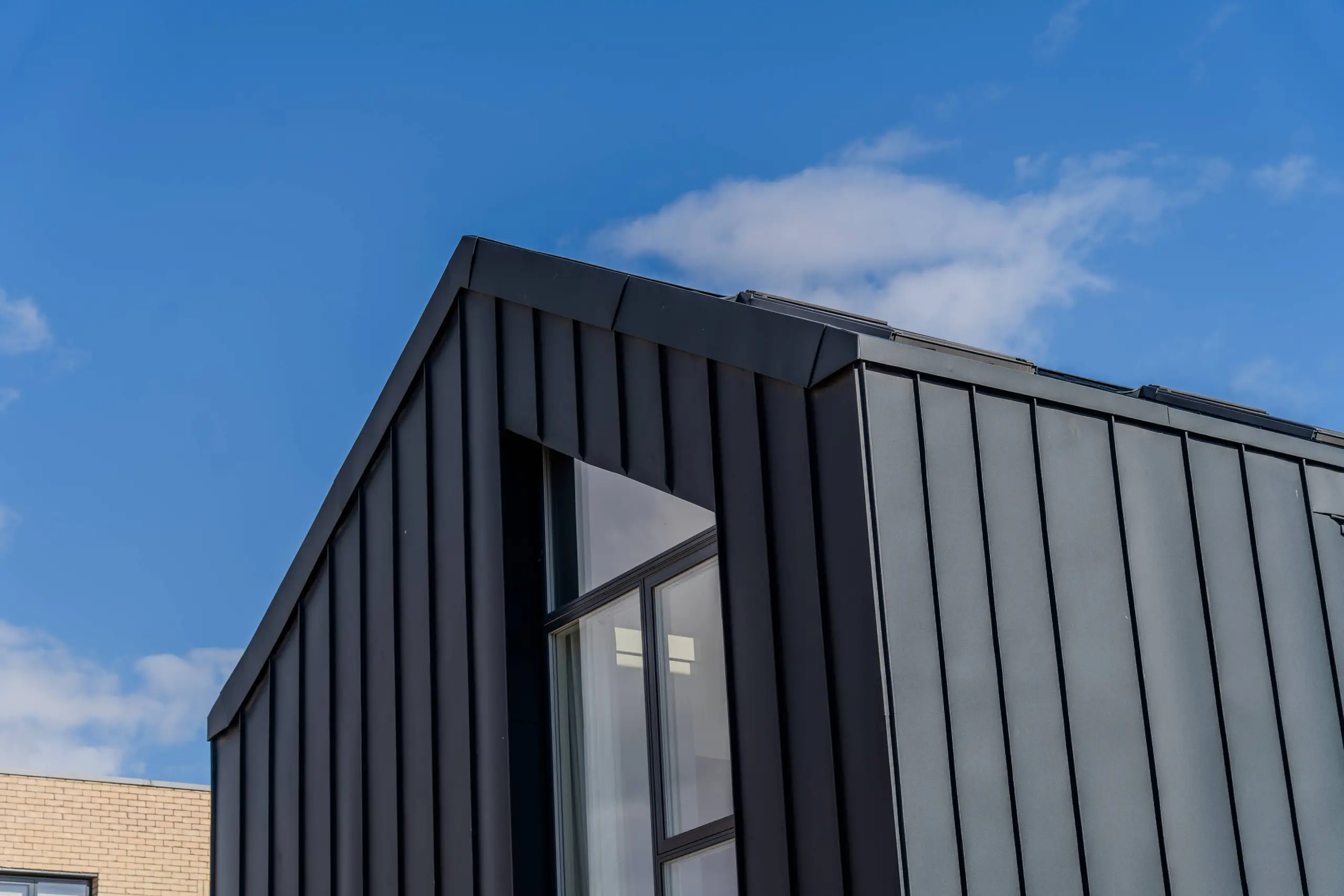 Modern building corner with black vertical cladding and large windows against blue sky