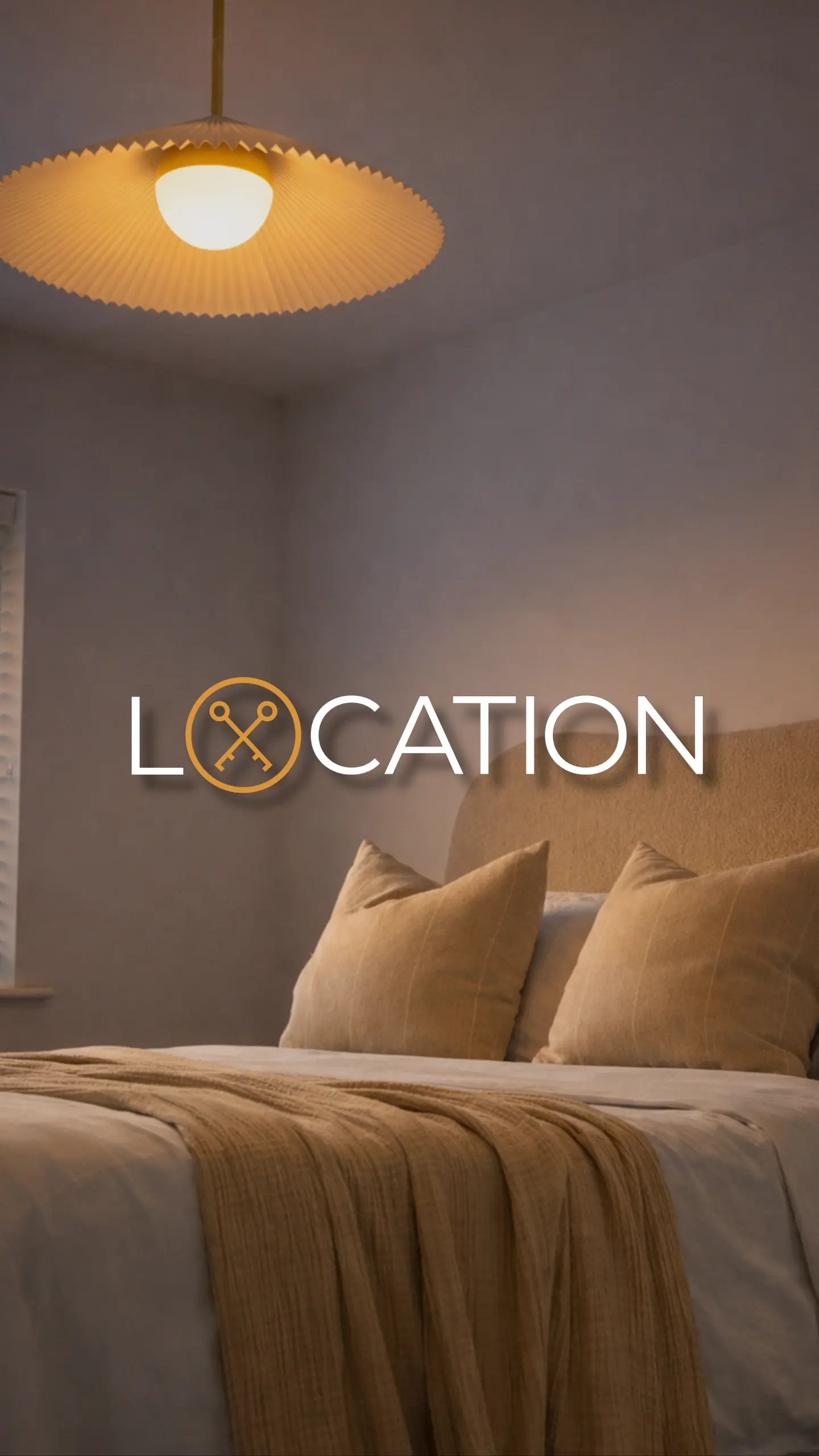 Bedroom with bed, tan pillows and bedding, pendant light overhead, and text reading 'LOCATION' with a crossed-keys icon
