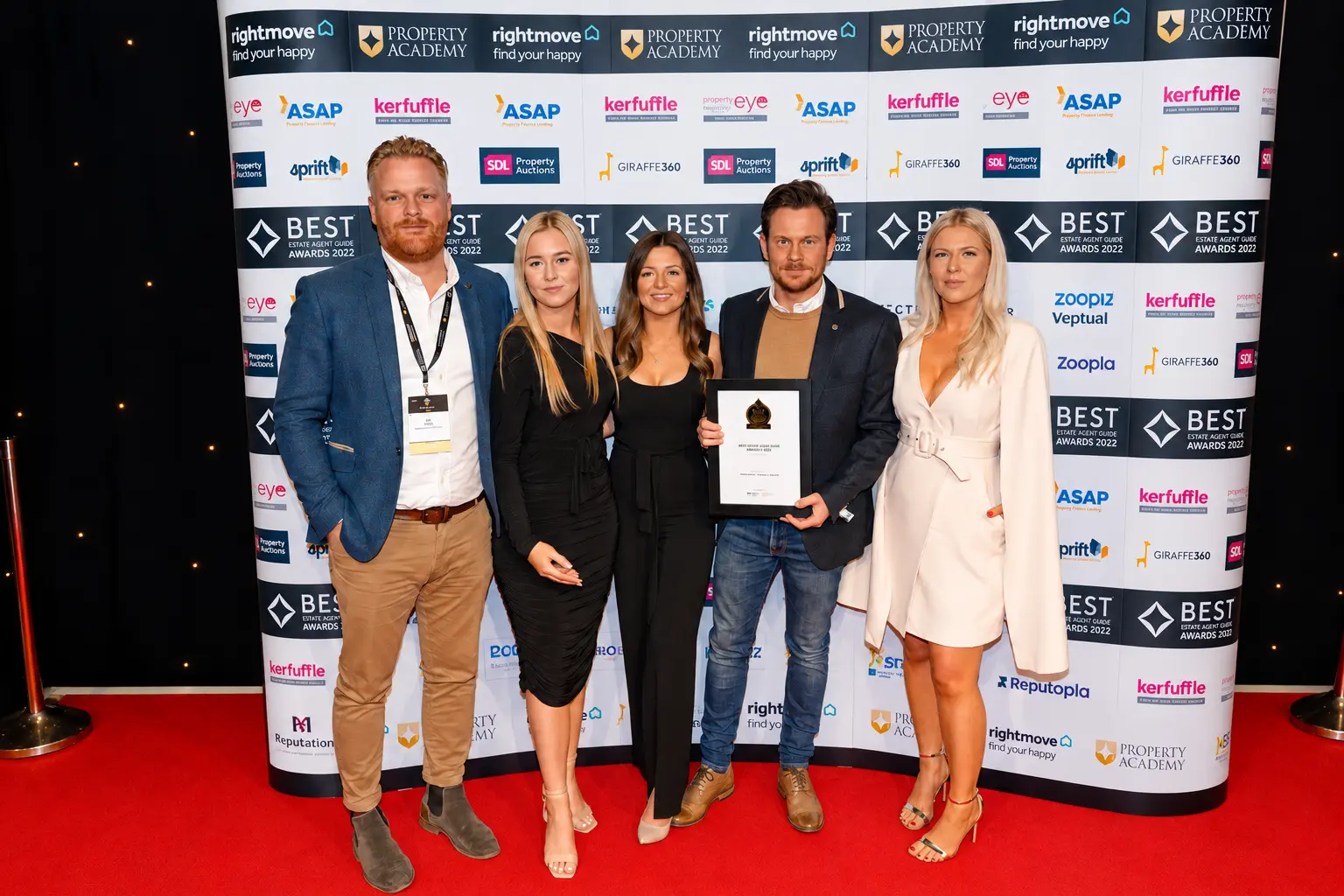 Five people standing on a red carpet in front a branded backdrop for Best Estate Agent Awards 2022, one person holding an award certificate