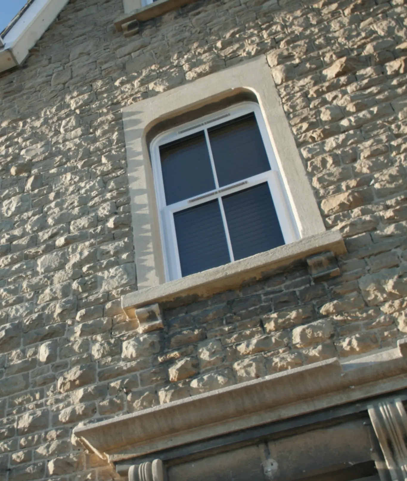 Stone-built house exterior with white-framed sash window with four panes and dark glass