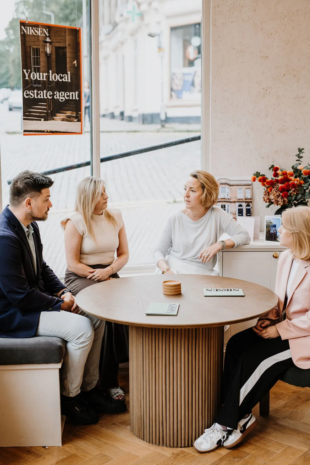 Estate agents meeting with clients at round table in bright office with Niksen branding visible on window
