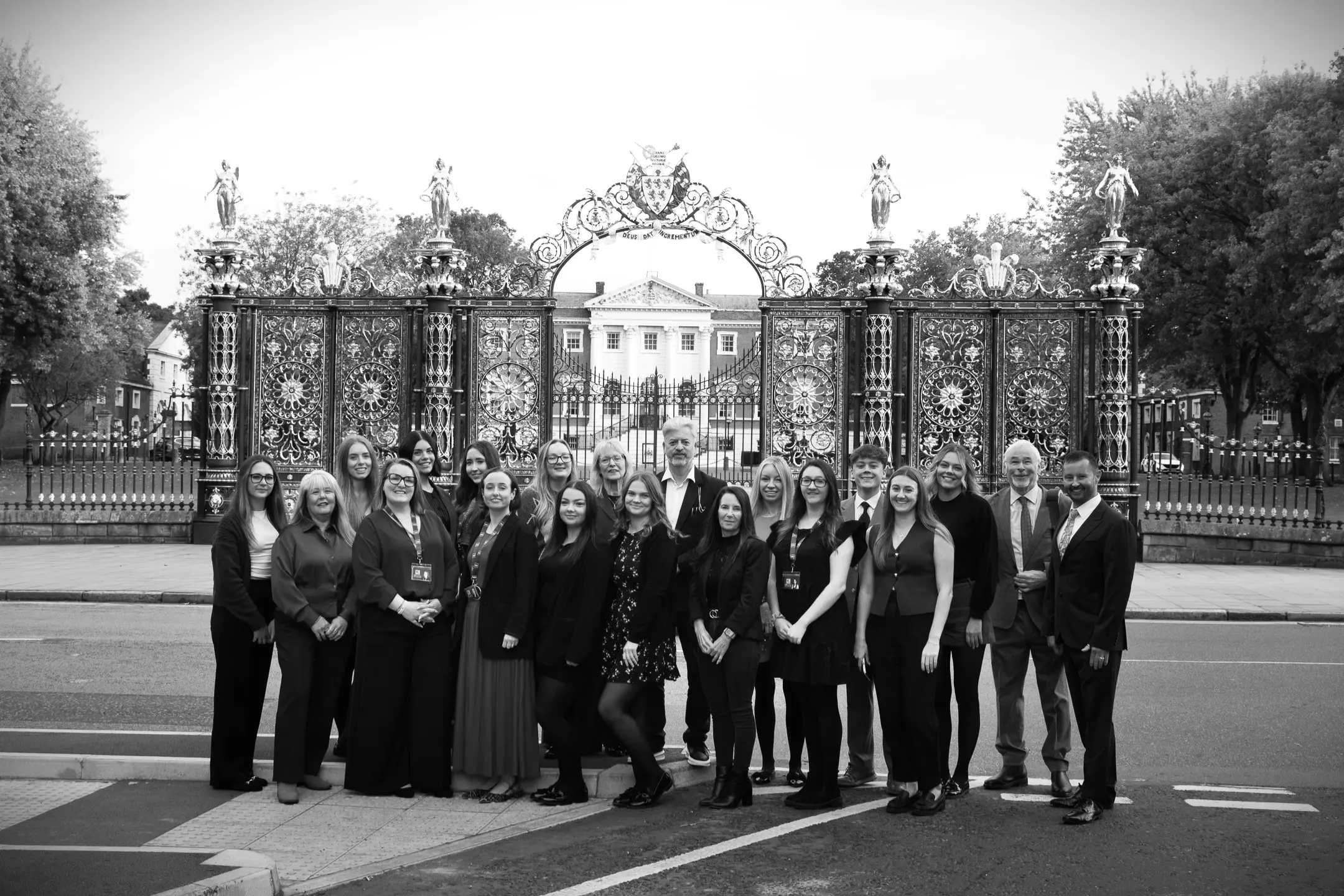 Group of people in formal business attire standing in front of ornate gates and a white building with columns