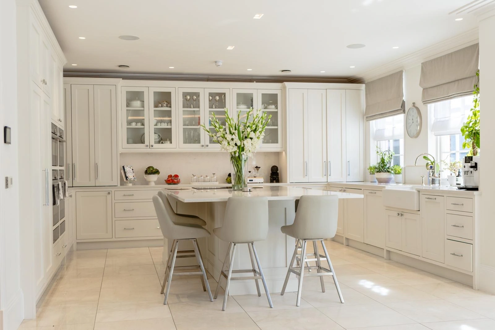 Modern kitchen with cream cabinetry, white countertops, central island with seating for three, and large windows overlooking garden