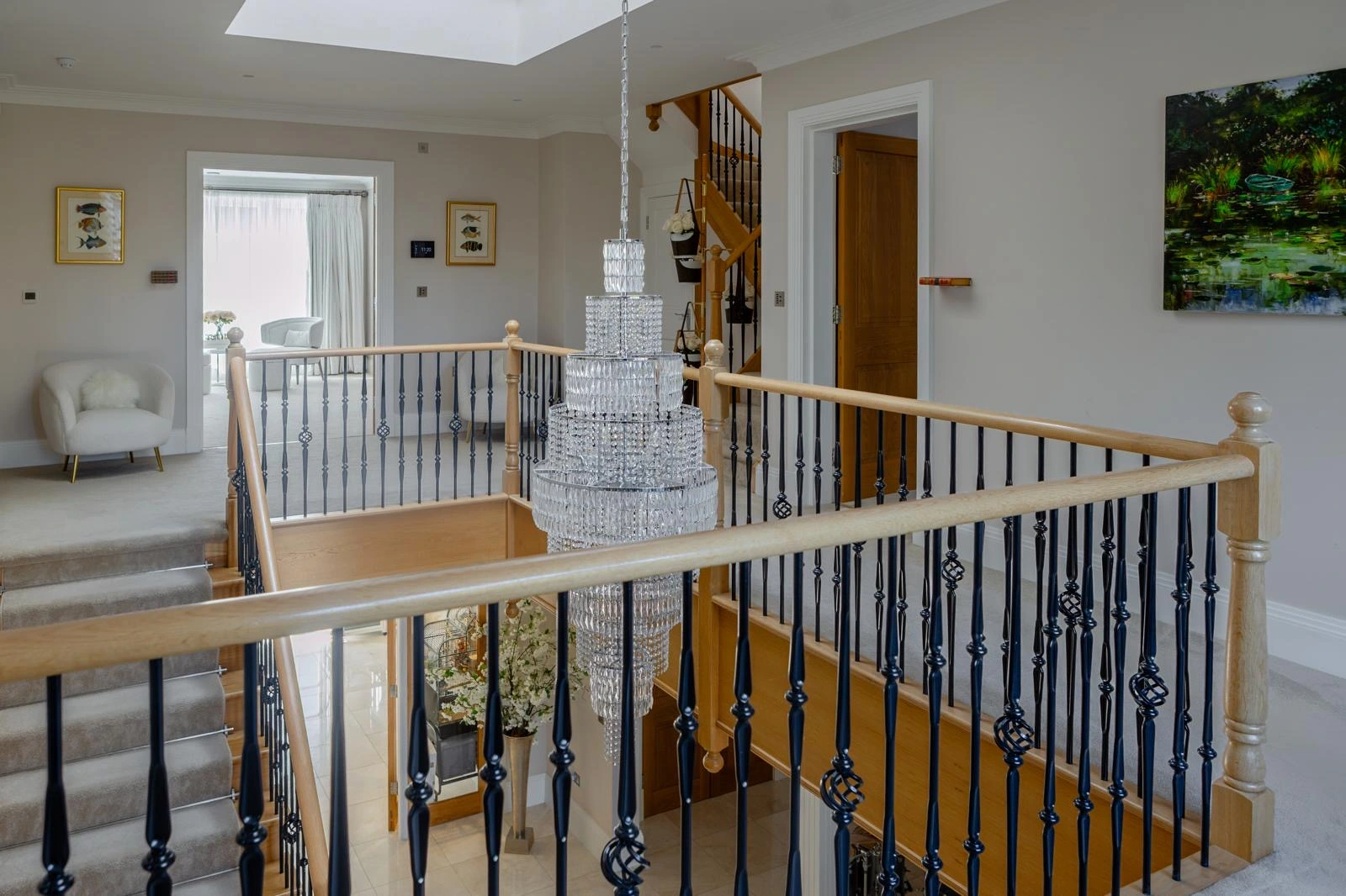 Landing with wooden handrail and black metal spindles, crystal chandelier, skylight, cream armchair, framed artwork, and doors leading to other rooms