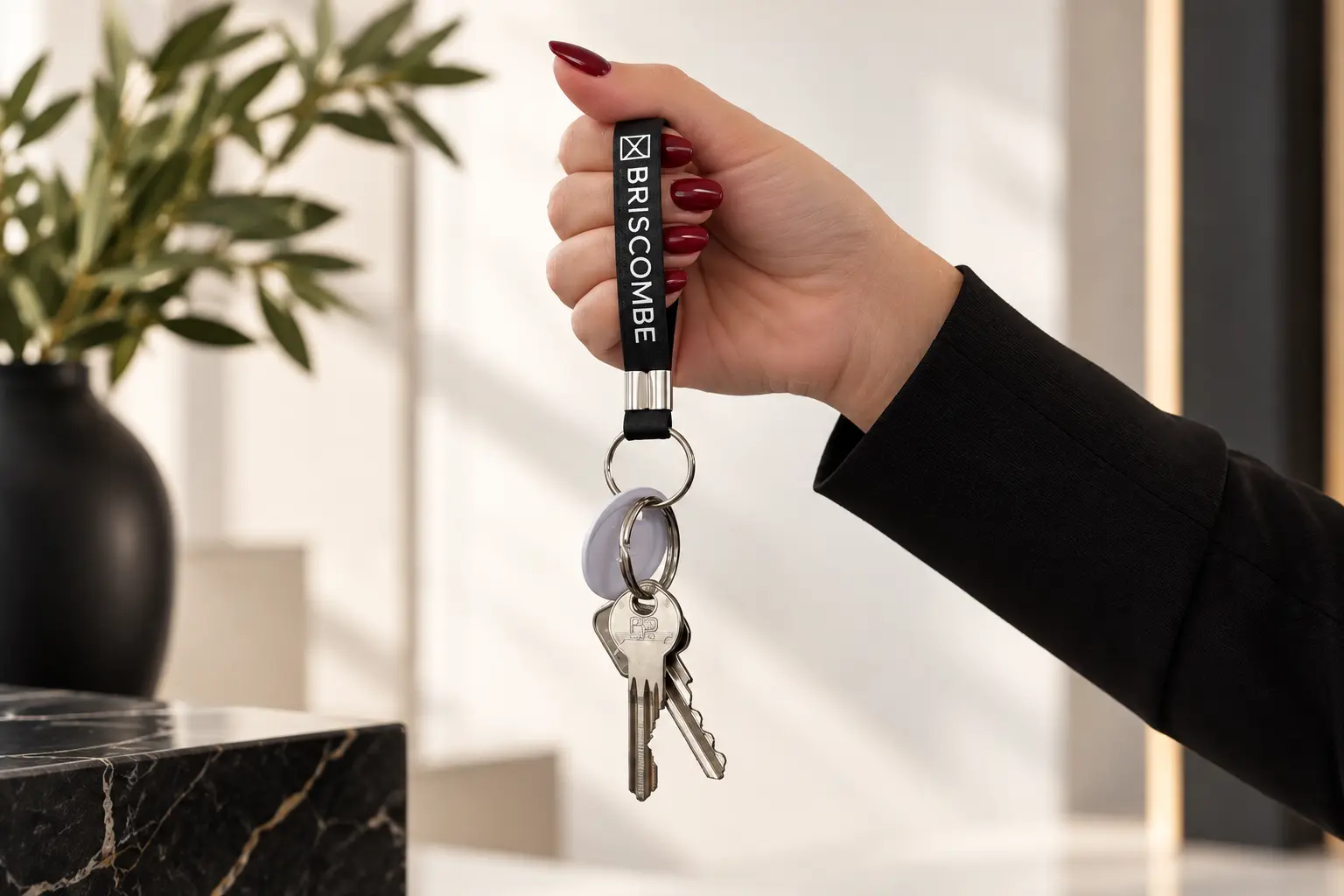 Hand holding a black keychain with 'BROSCOMBE' text and a property key attached