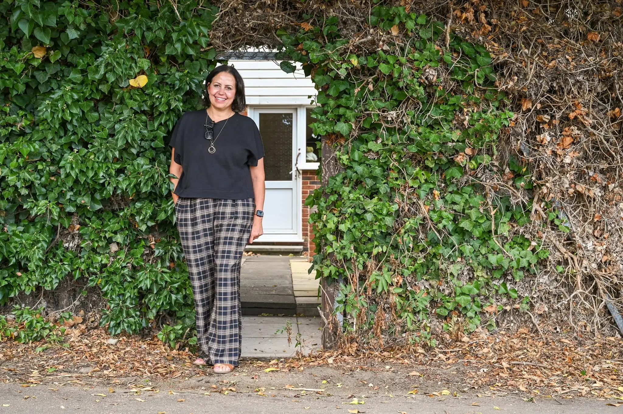 Woman standing in front of a white door framed by ivy-covered walls on a brick building