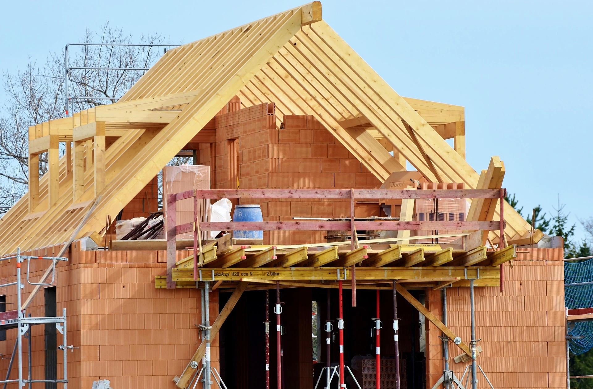 House under construction with red brick walls, timber roof frame, and metal scaffolding