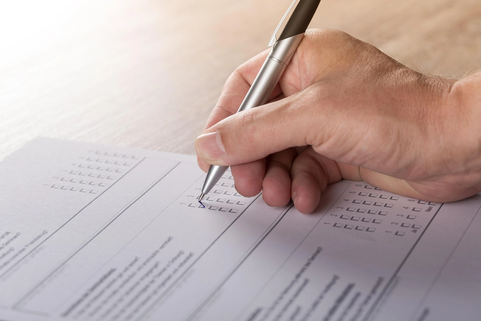 Hand holding a pen marking checkboxes on a form or survey document