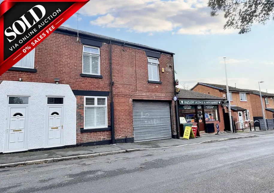Red brick building with white-painted ground floor, garage door, and shop frontage. Red banner in top left corner reads 'SOLD VIA ONLINE AUCTION 0% SALES FEE'. Street view with neighbouring shops and buildings.