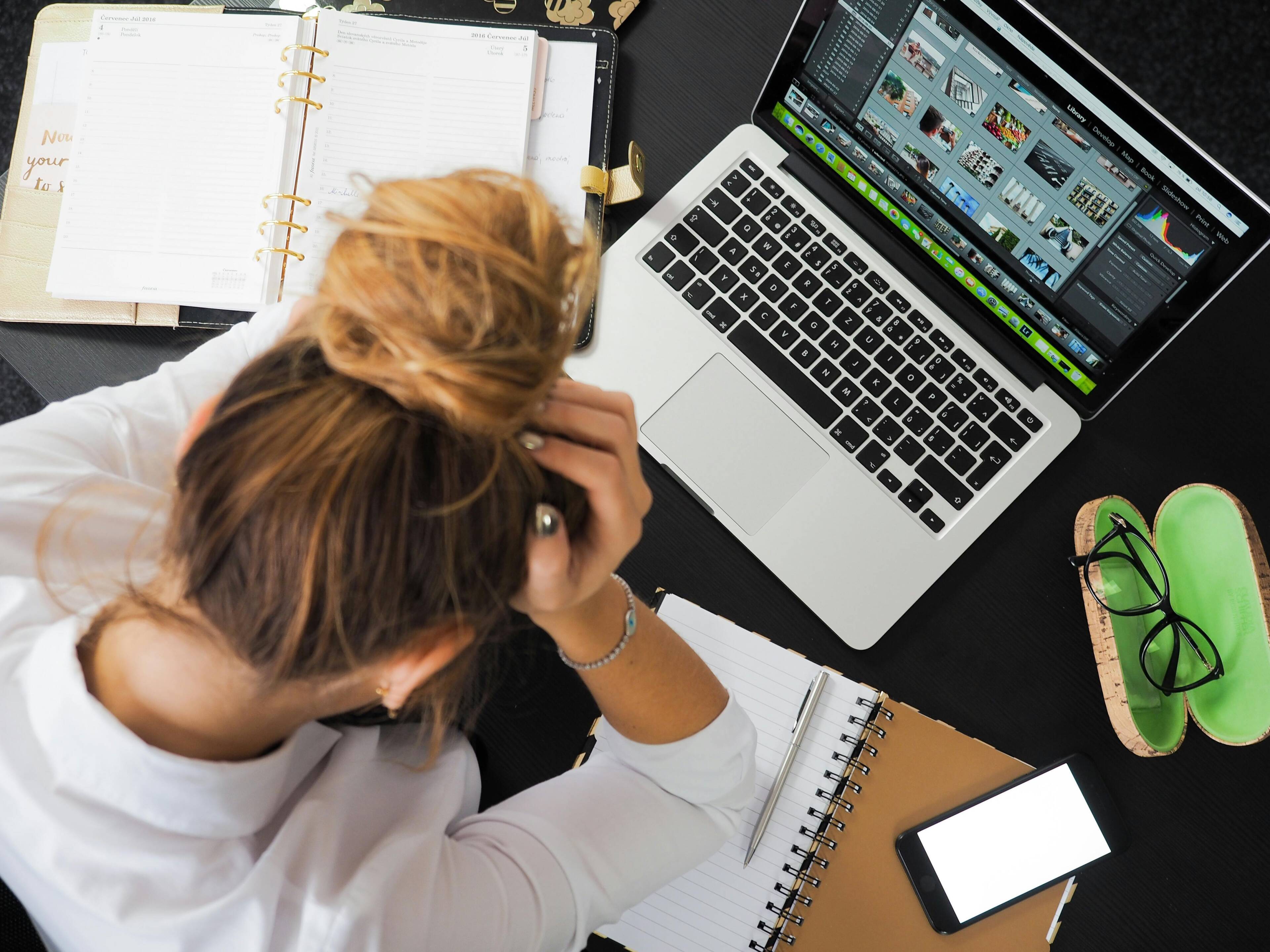 Stressed woman sitting at a desk with a laptop and notebooks