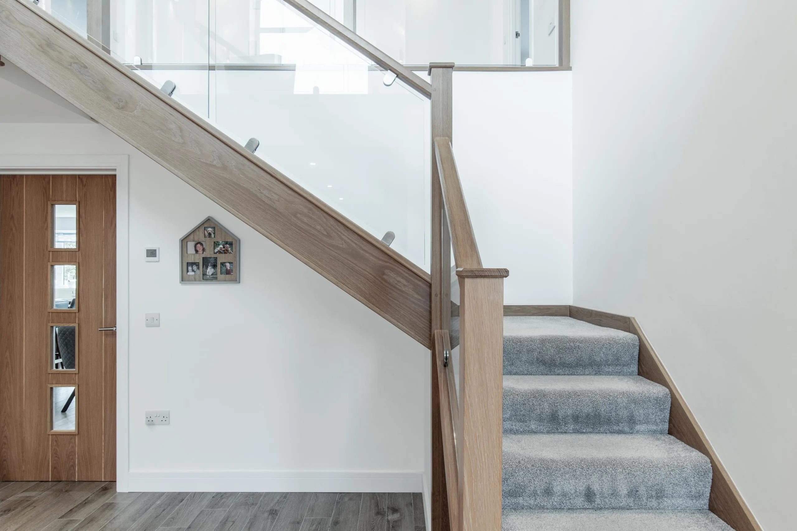 Modern staircase with light wood handrail, glass balustrade, and grey carpet treads, leading to upper level with skylights