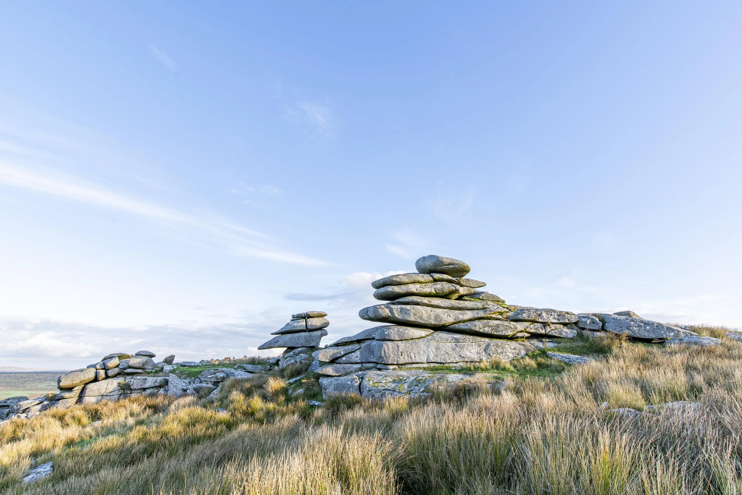 Stacked rocks on moorland with dry grass and blue sky