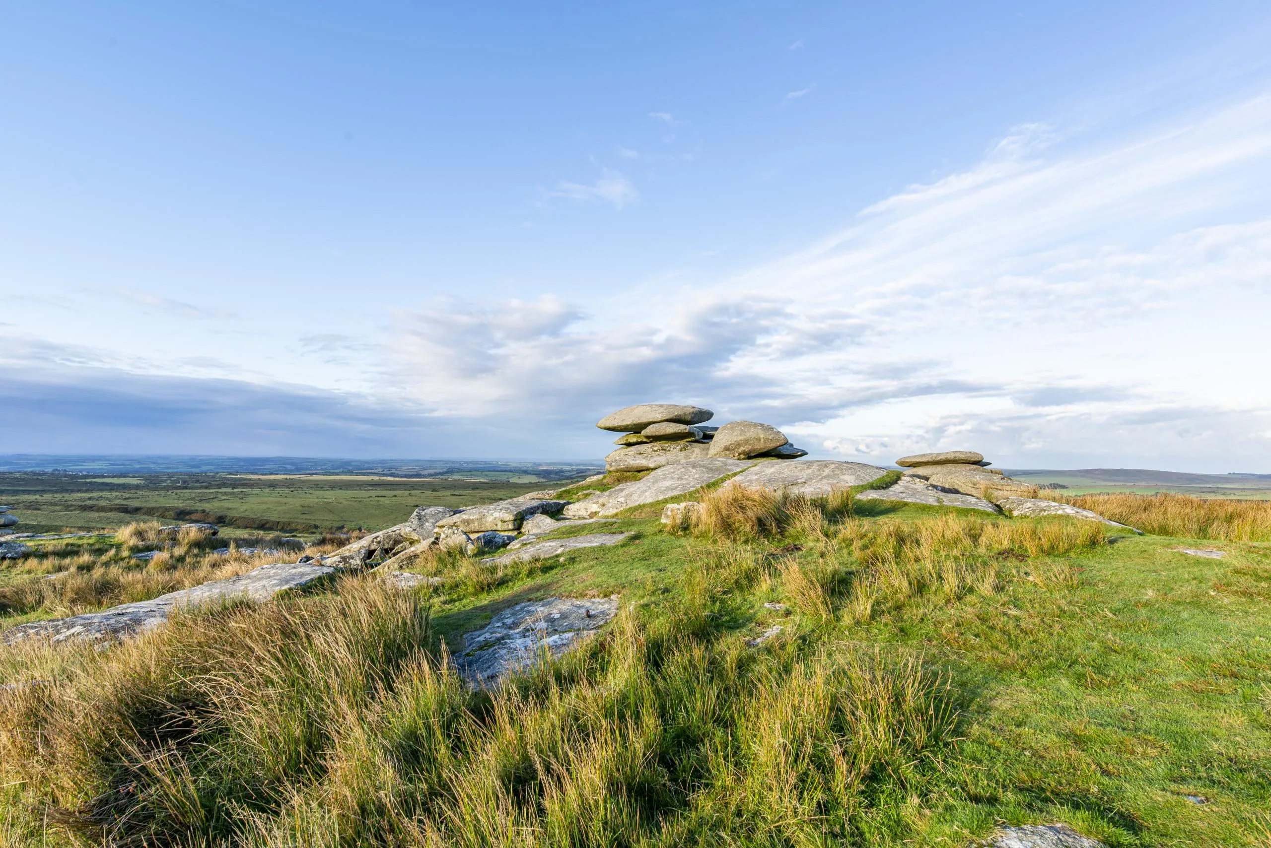 Rocky outcrop with stacked boulders on moorland, grassy hillside with expansive valley view below