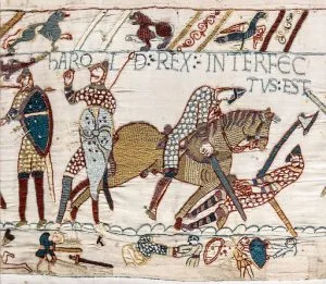 Medieval embroidery showing figures on horseback and on foot, with Latin text including "INTERFEC" visible at top