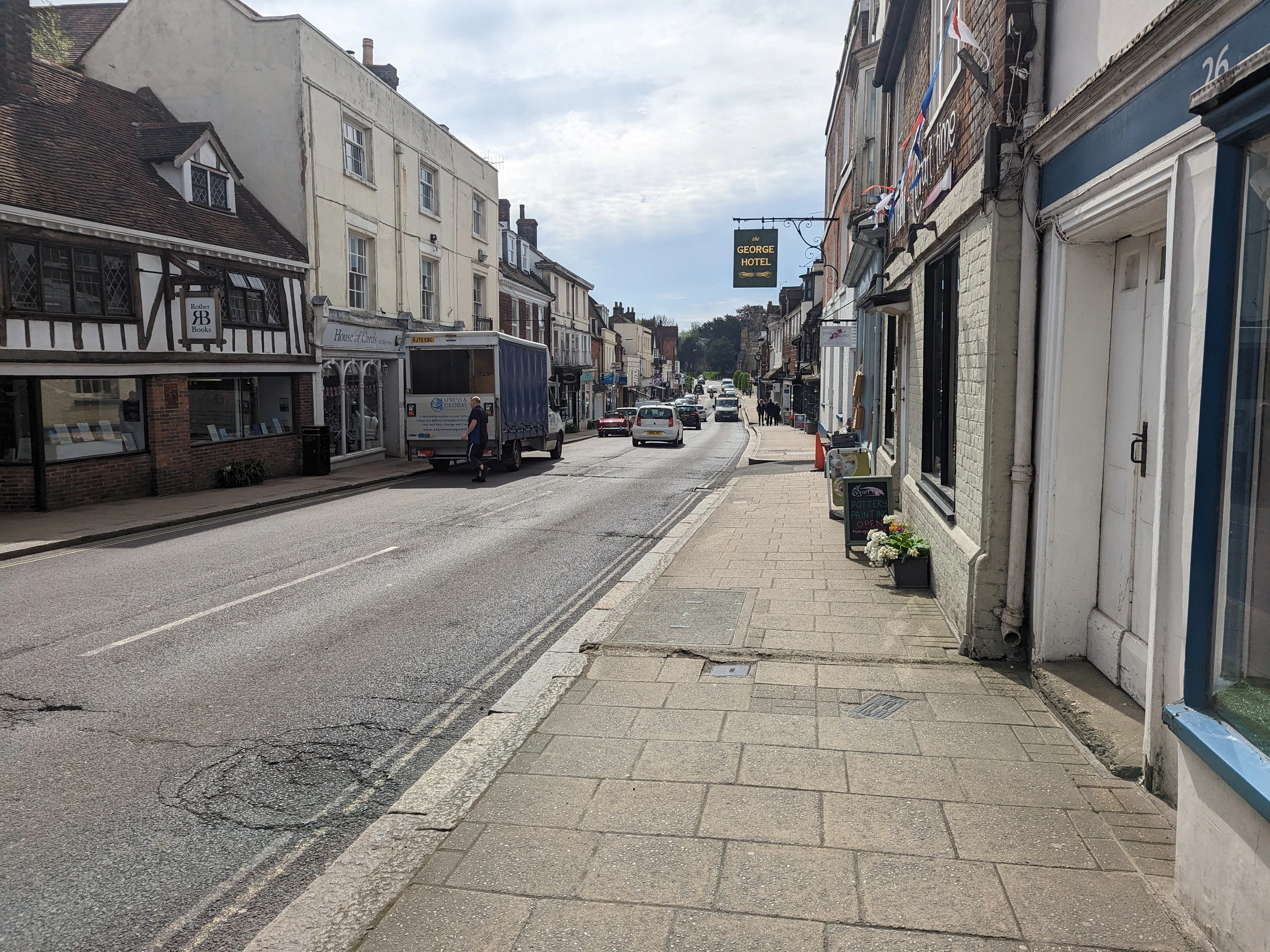 High street with period buildings, shops, and George Hotel sign; parked vehicles and pedestrians visible