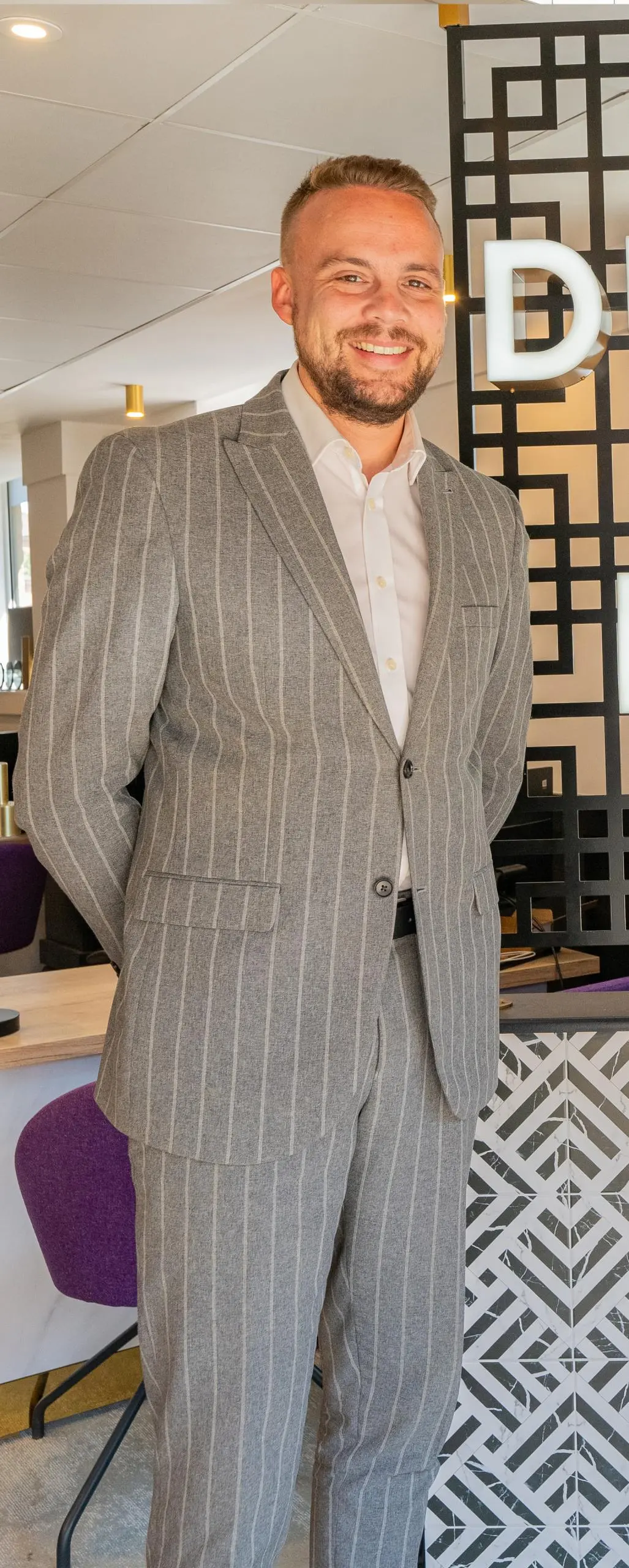 Man in grey pinstriped suit and white shirt standing in modern office interior
