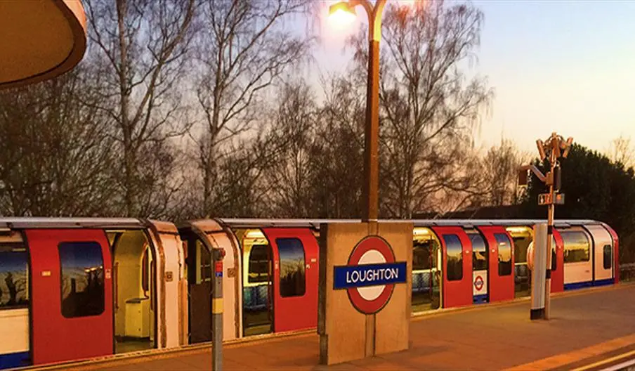 London Underground train at Loughton station at dusk, with bare trees and street lamp visible