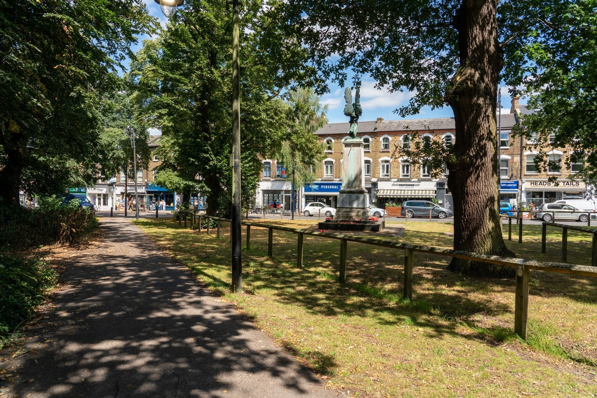 Public square with trees, benches, and a statue, overlooking brick buildings and shops with parked cars