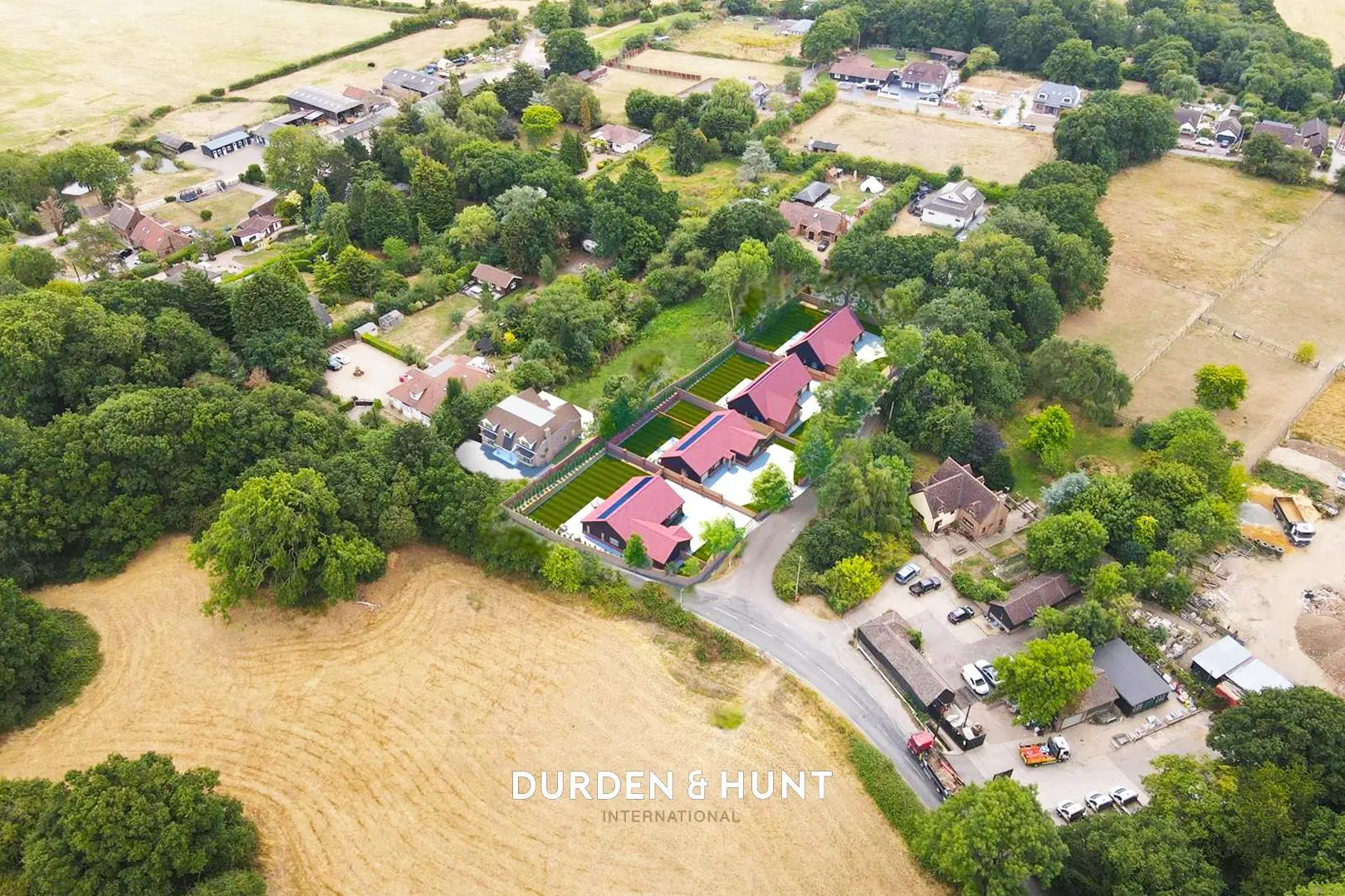 Aerial view of rural residential development with four modern houses with red roofs, surrounded by trees and farmland