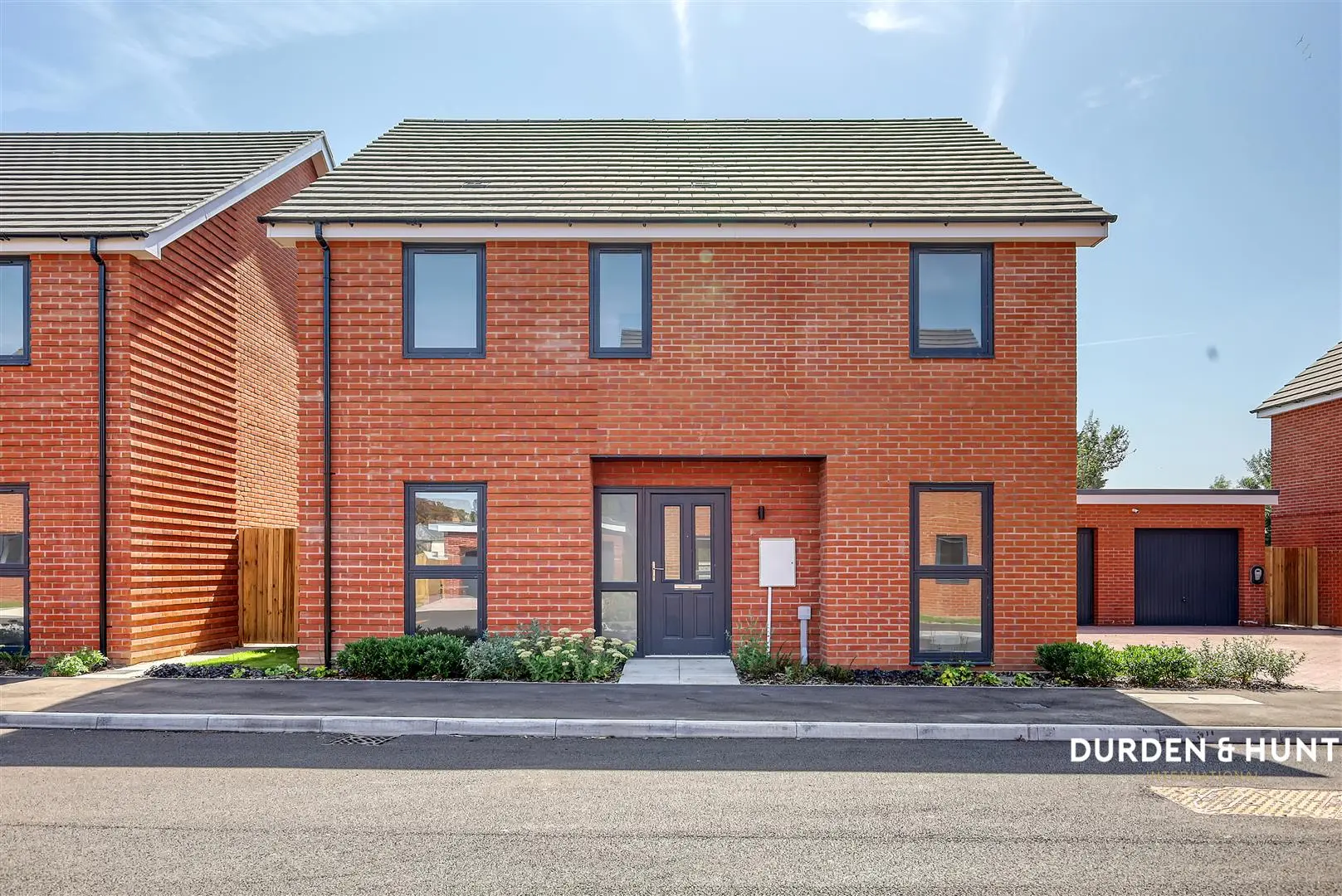Modern red brick house with pitched roof, dark windows and door, front garden with shrubs, Durden & Hunt branding visible