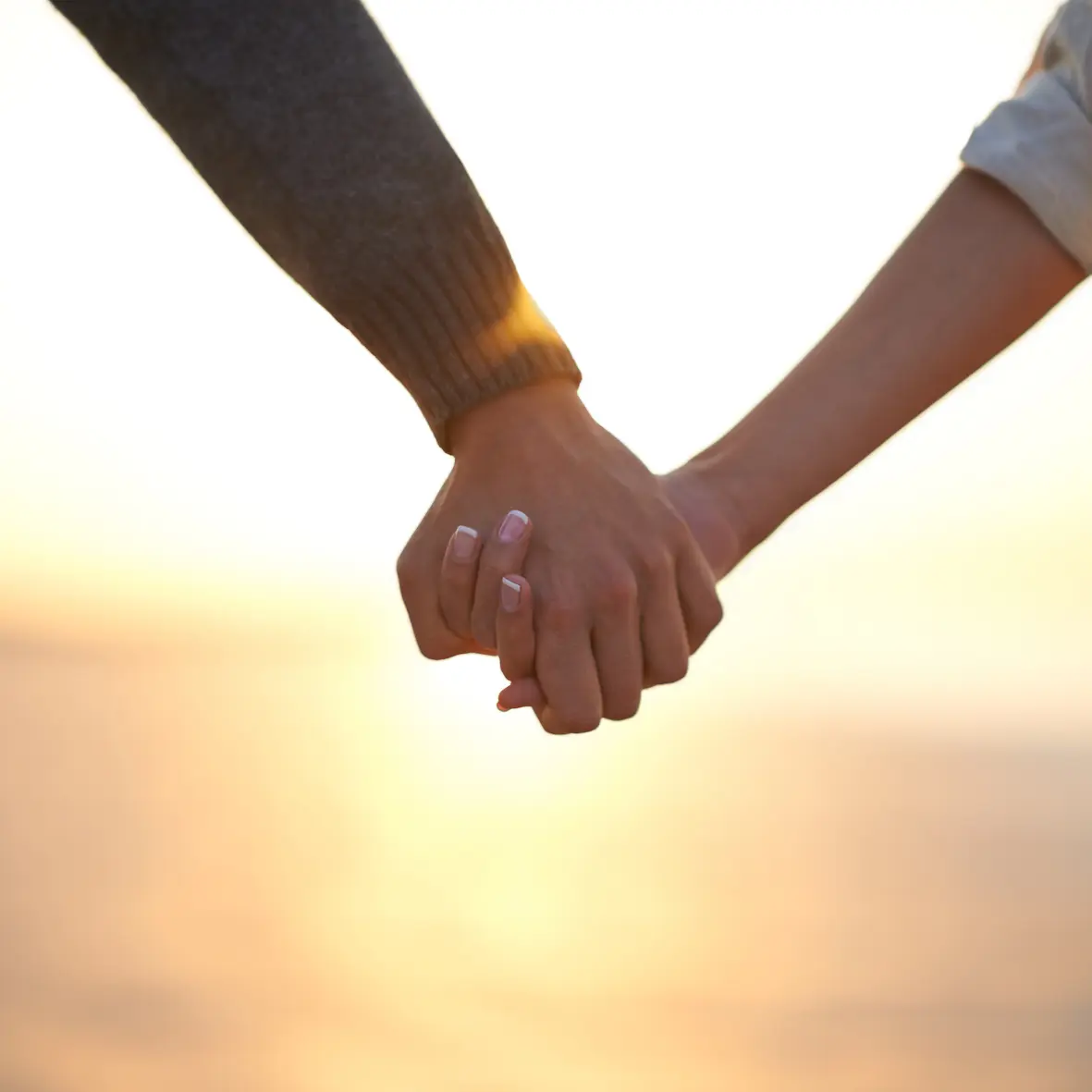 Two people holding hands against a sunset sky