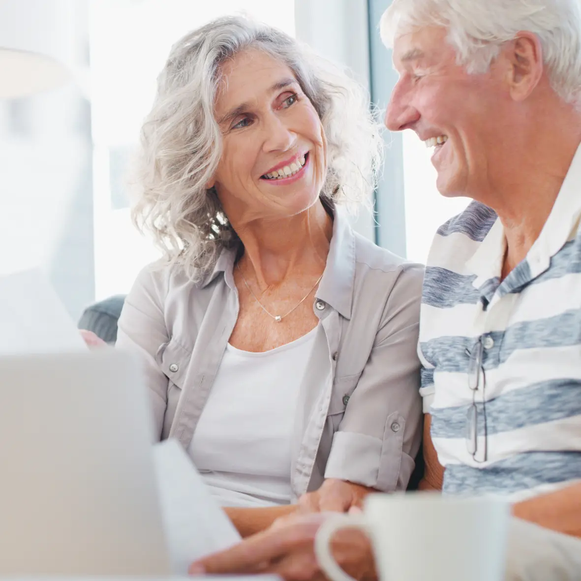 Two older adults smiling while looking at a laptop together indoors