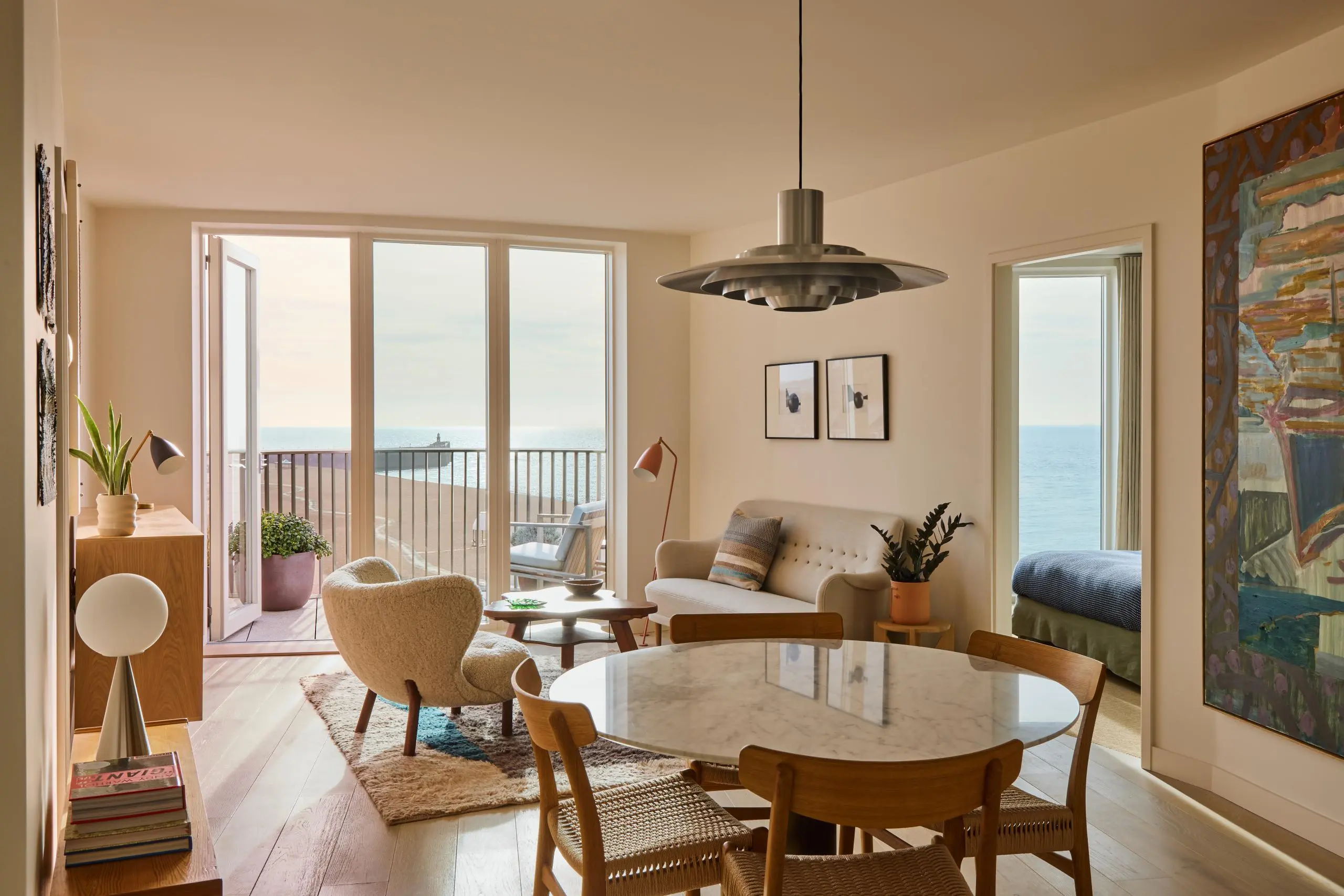 Modern apartment interior with dining table, seating area, and sea view through glass doors opening onto a balcony