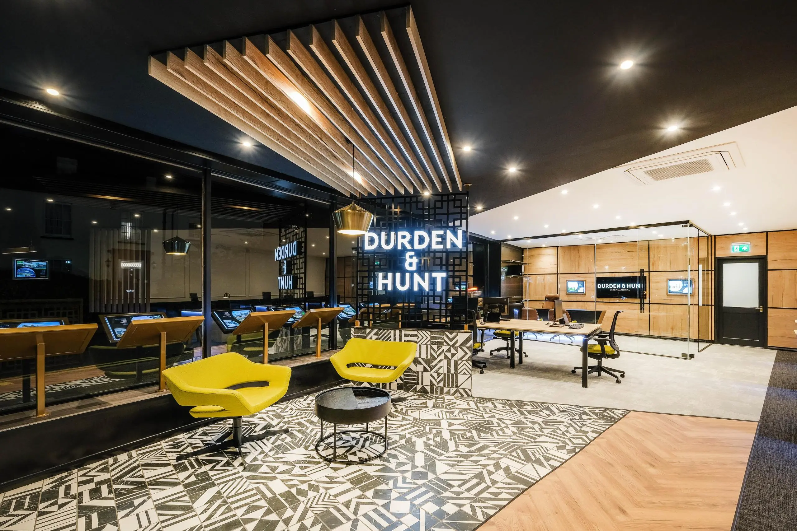 Durden & Hunt office interior with yellow chairs, geometric patterned flooring, wooden ceiling slats, and neon signage