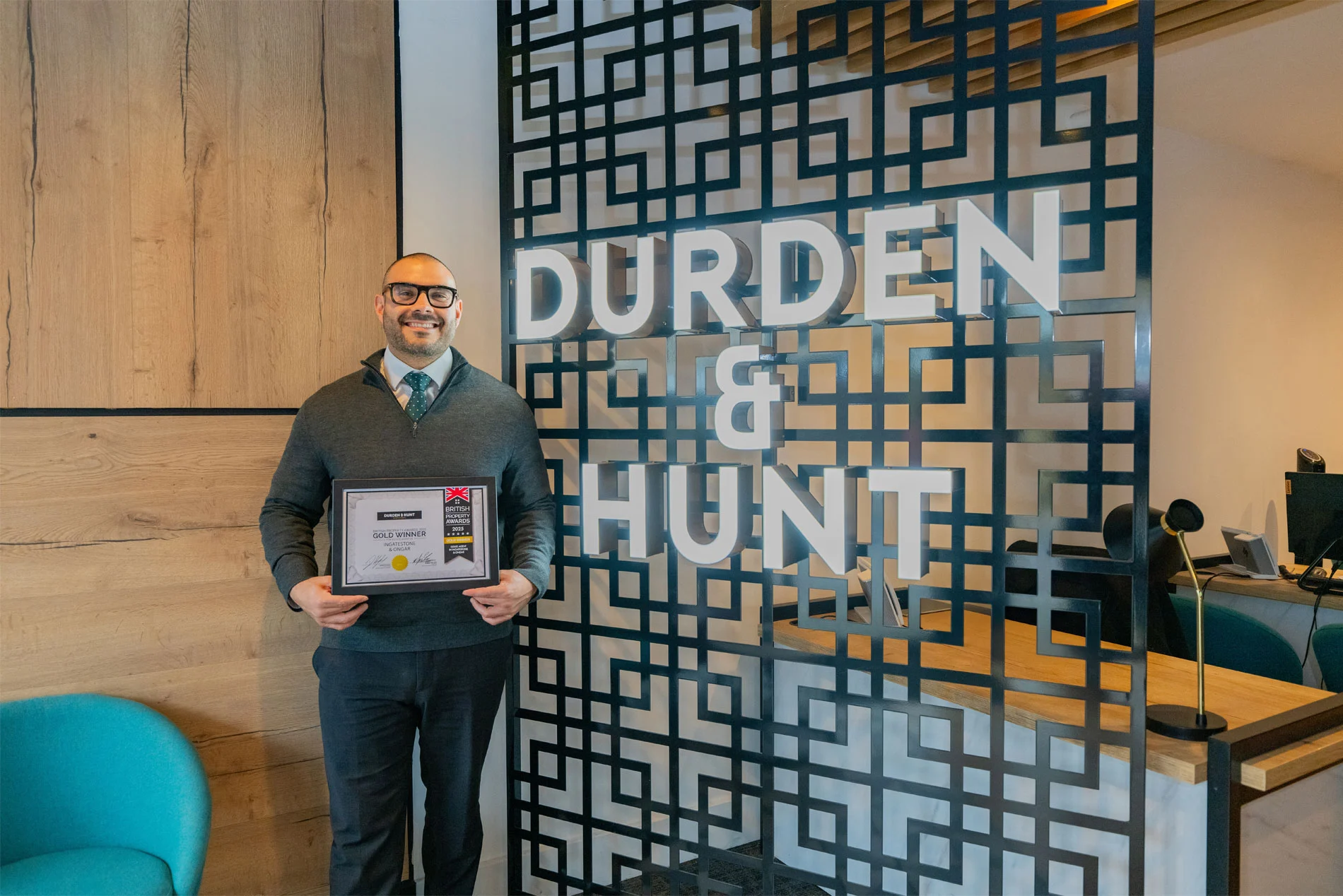 Man holding a gold winner certificate in front of Durden & Hunt office signage