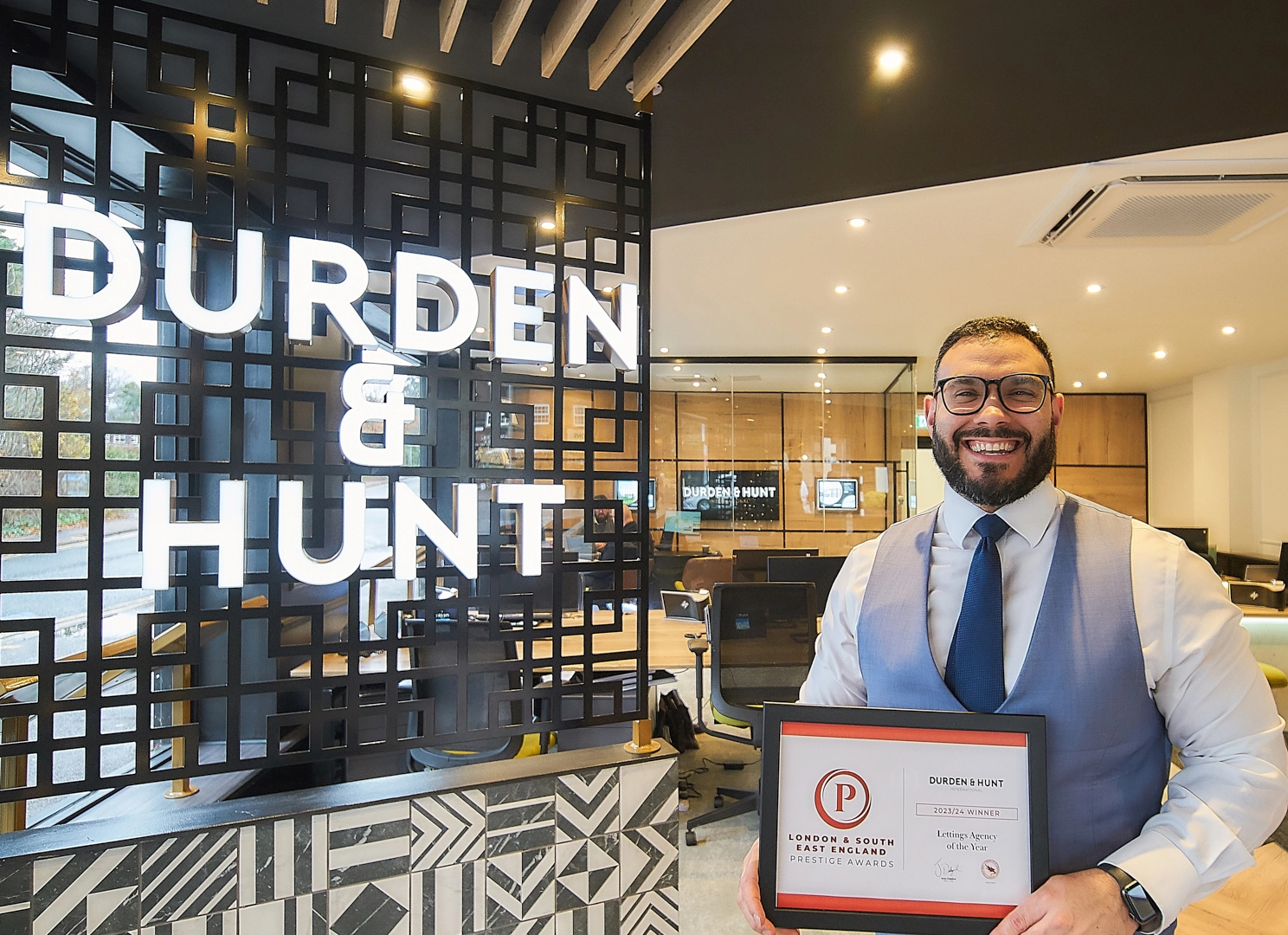 Man in white shirt and blue tie holding award plaque inside Durden & Hunt estate agency office