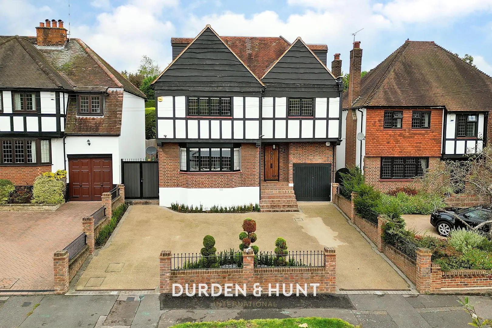 Mock Tudor and brick houses with black and white timber framing, pitched roofs, and brick driveways. Durden & Hunt International branding visible.