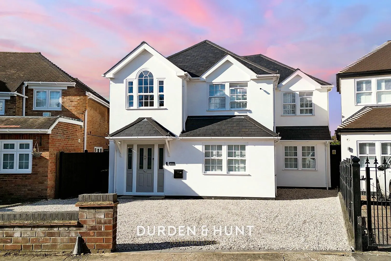 Modern white two-storey detached house with black roof, arched window, driveway and brick boundary wall