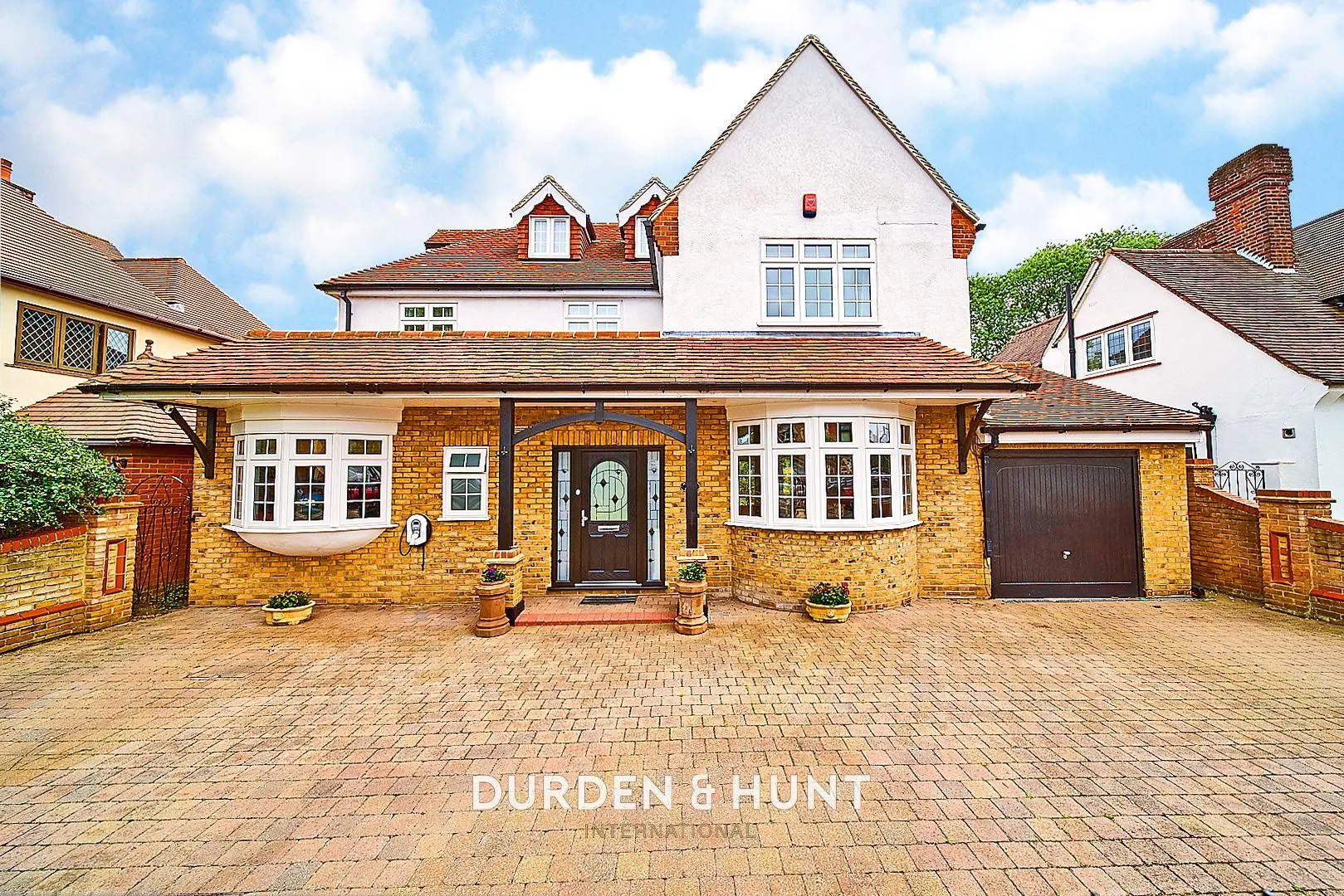 Brick and white rendered detached house with pitched roof, bay windows, dark brown front door, and brick driveway