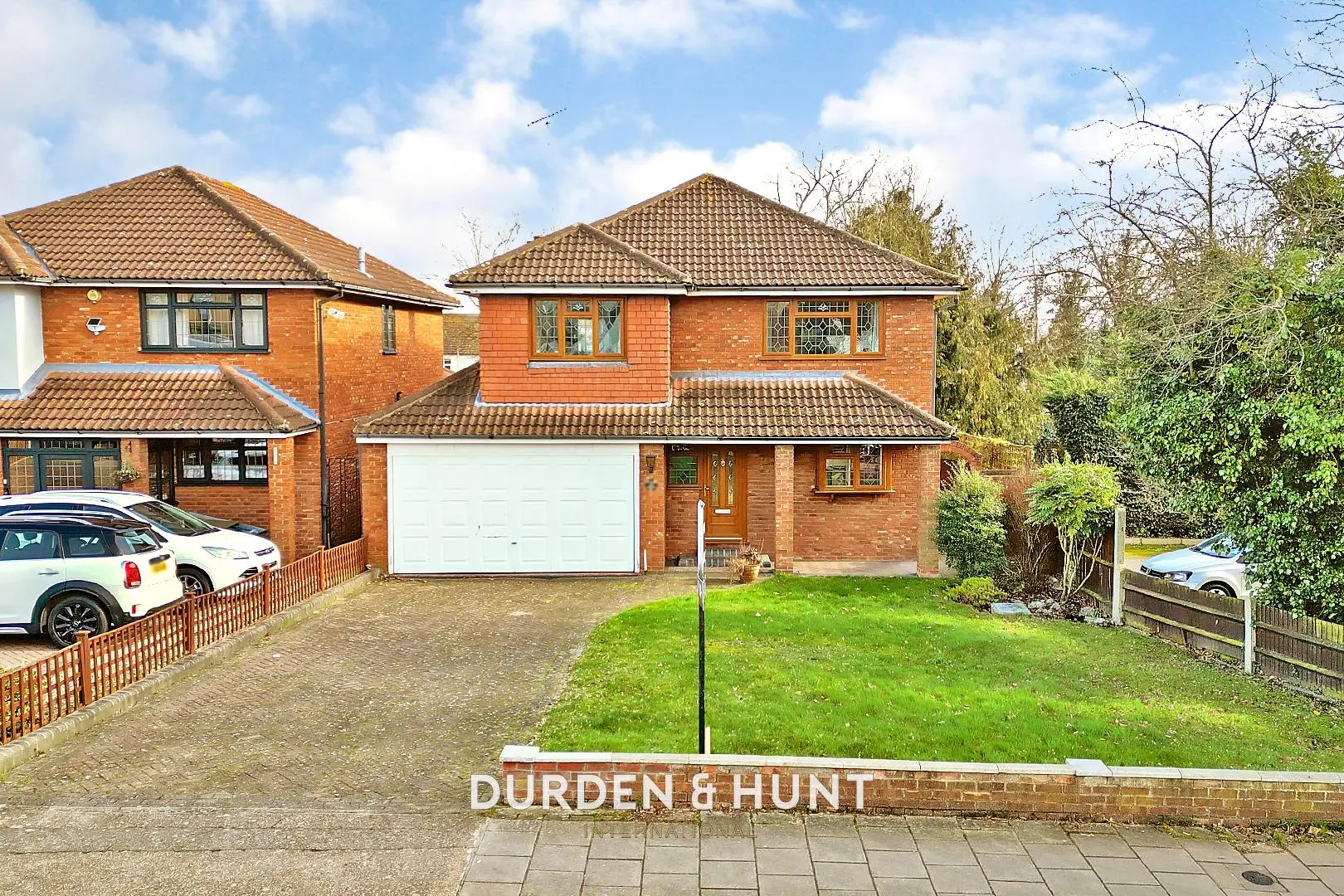 Red brick detached house with white garage door, driveway, and front garden with lawn and fence