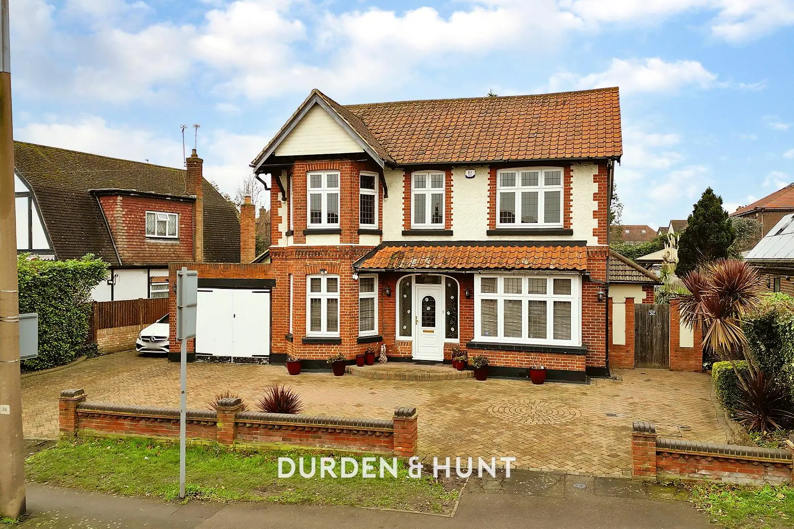 Two-storey red brick house with white-painted upper storey, tiled roof, driveway and front garden