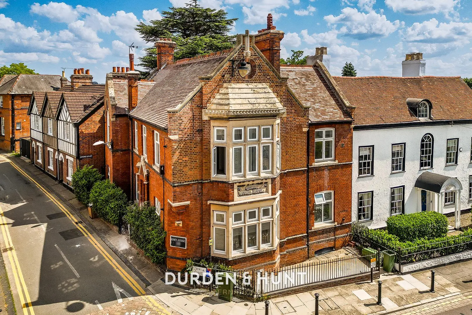 Row of Victorian brick buildings on a street corner, including a prominent red-brick corner property with white-framed bay windows and slate roof. Durden & Hunt branding visible.