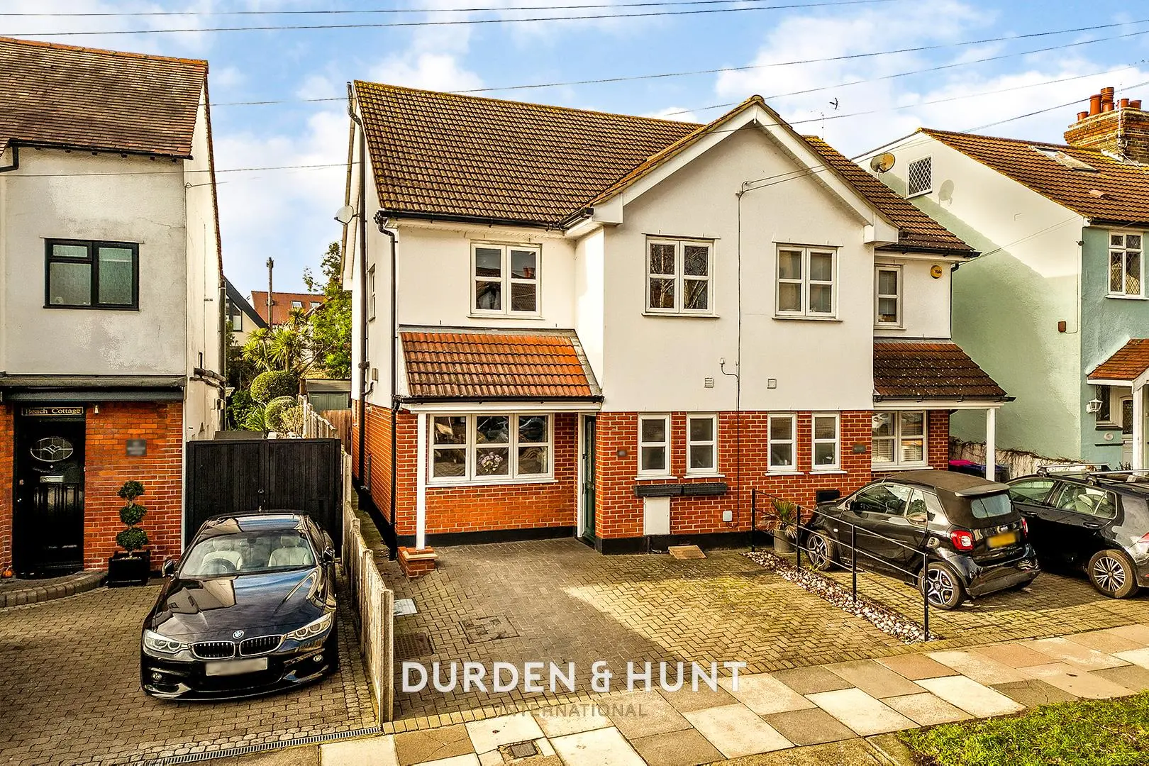 Row of residential properties with cream and white rendered upper storeys and red brick lower sections, parked cars on paved driveway, Durden & Hunt branding visible