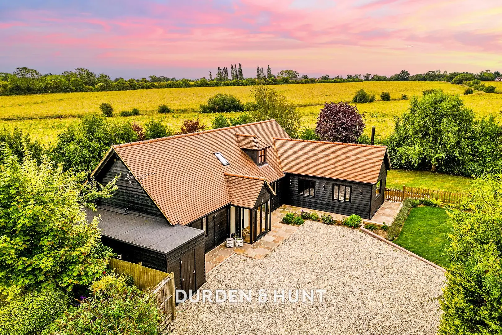 Modern black barn conversion with terracotta roof, surrounded by yellow rapeseed field and green hedgerows